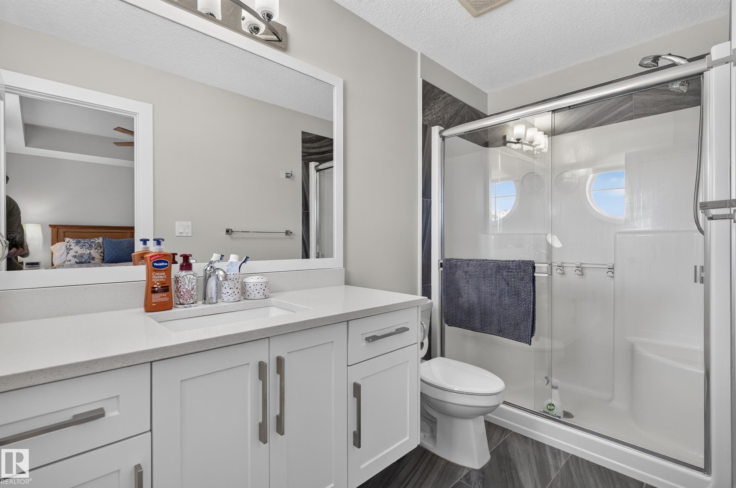 Bathroom featuring a white shaker-style vanity with a solid surface countertop, an undermount rectangular sink, a framed mirror, and a walk-in shower with glass sliding doors and integrated shelving - 798 Berg Loop, Leduc, AB