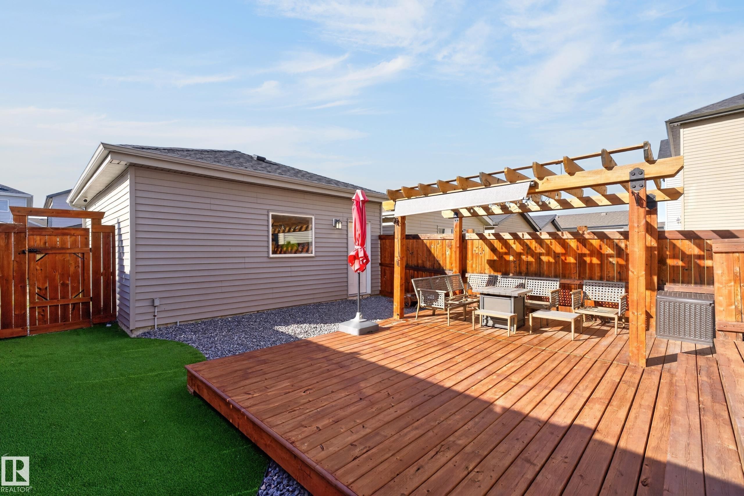 Backyard featuring a wood deck, integrated timber pergola, artificial turf lawn, decorative stone perimeter, and wood privacy fencing - 798 Berg Loop, Leduc, AB