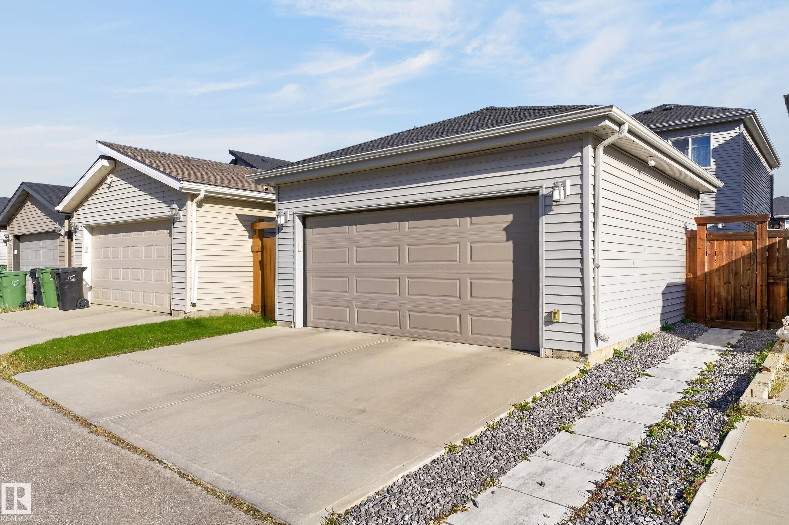 Detached garage featuring horizontal siding, a paneled overhead door, a concrete driveway, and an attached wood privacy gate - 798 Berg Loop, Leduc, AB