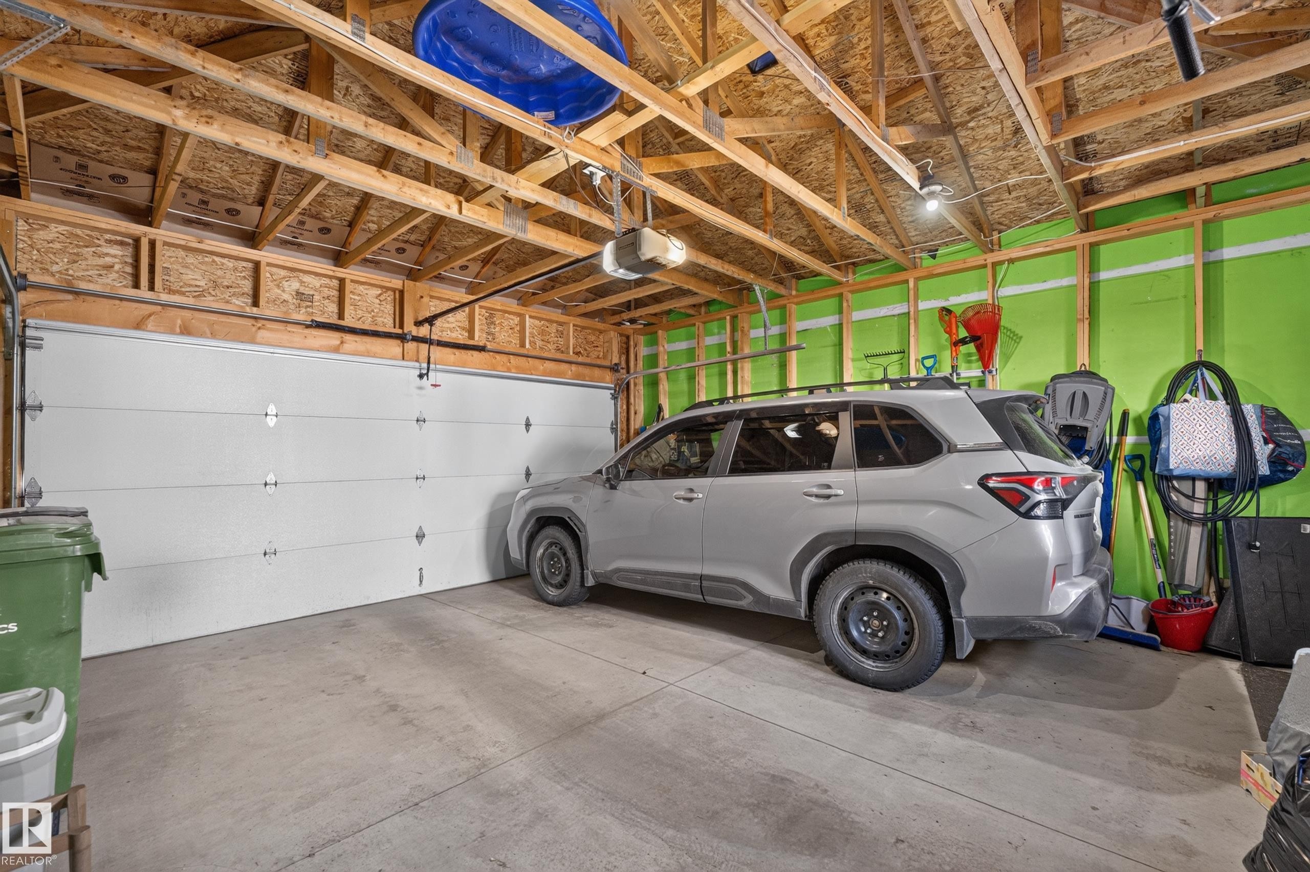 Garage space featuring a concrete floor, high vaulted ceiling with exposed wooden trusses, an automated overhead door, and painted wall panels - 798 Berg Loop, Leduc, AB