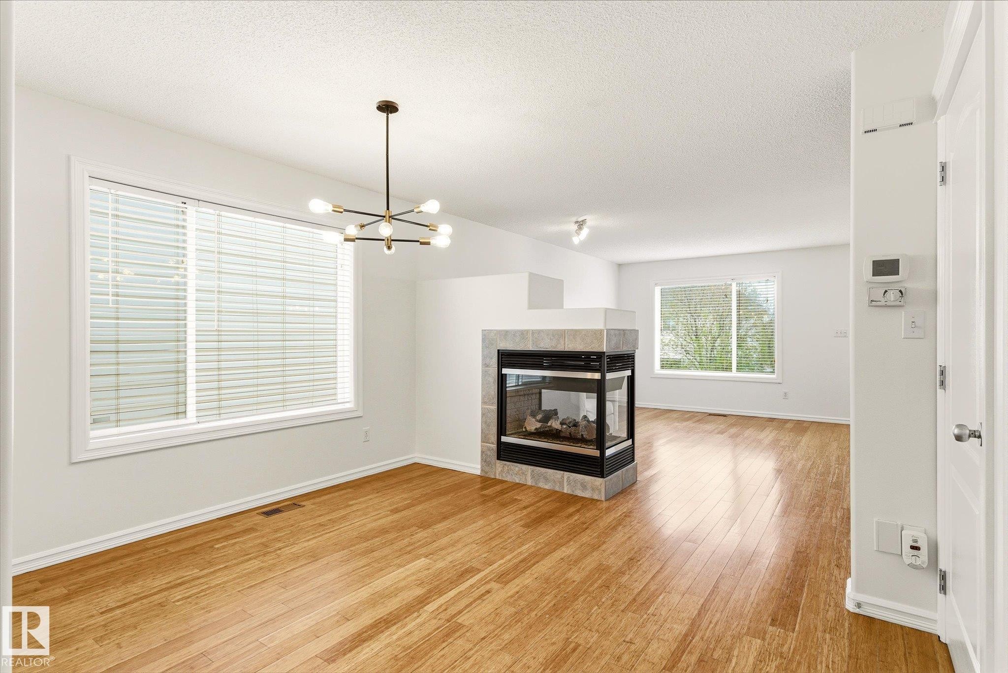 Wood-finish flooring throughout, featuring a modern chandelier, large windows with blinds, and a built-in fireplace with a tiled surround - 2550 Rabbit Hill Road Nw, Edmonton, AB