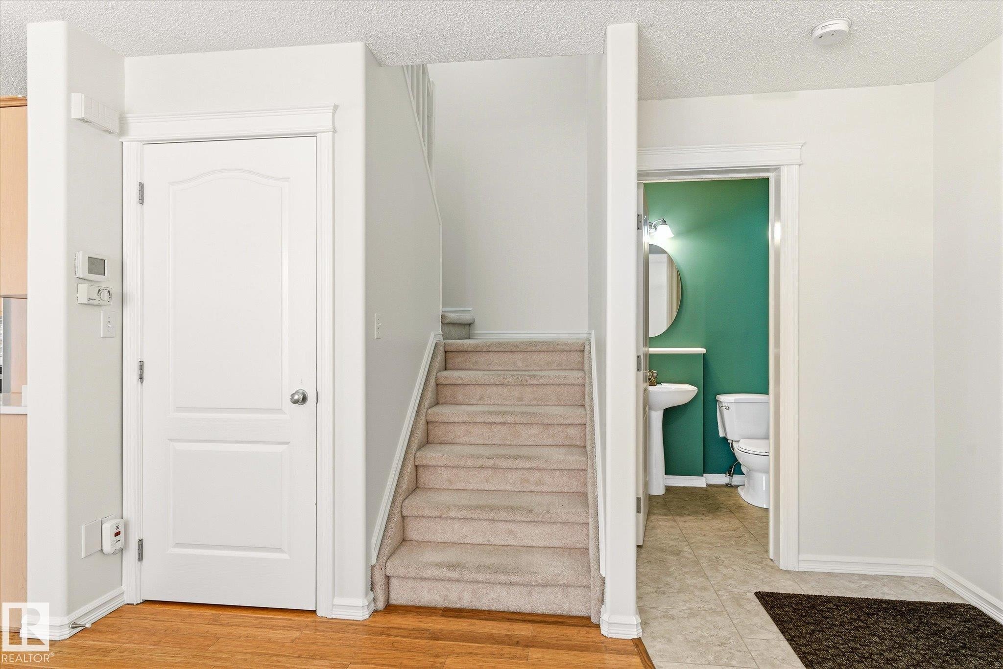 Wood-finish flooring, a carpeted staircase, and a pedestal sink with a circular mirror - 2550 Rabbit Hill Road Nw, Edmonton, AB