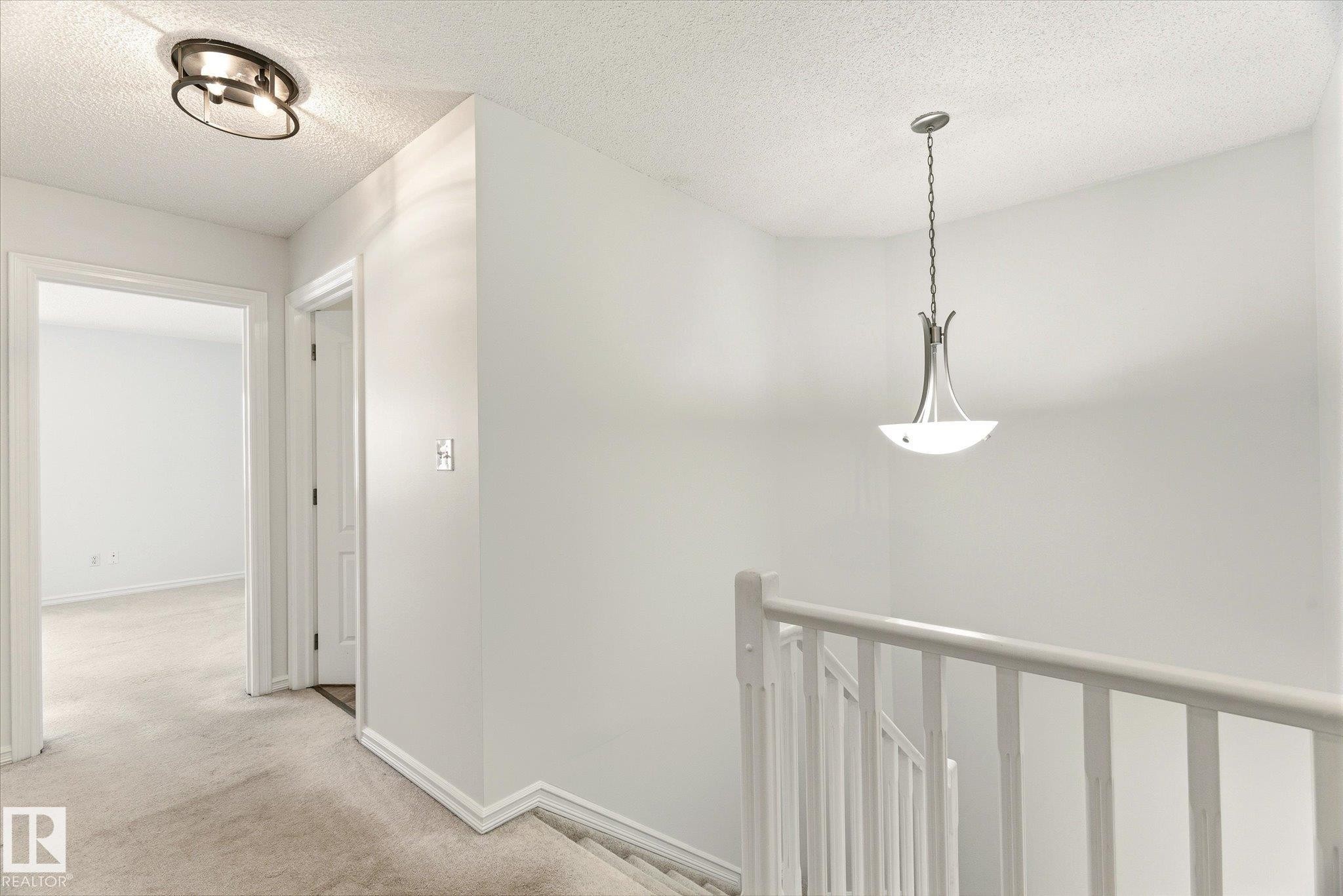 Hallway with neutral carpeting and white painted walls, featuring a semi-flush mount ceiling light and a contemporary pendant light - 2550 Rabbit Hill Road Nw, Edmonton, AB