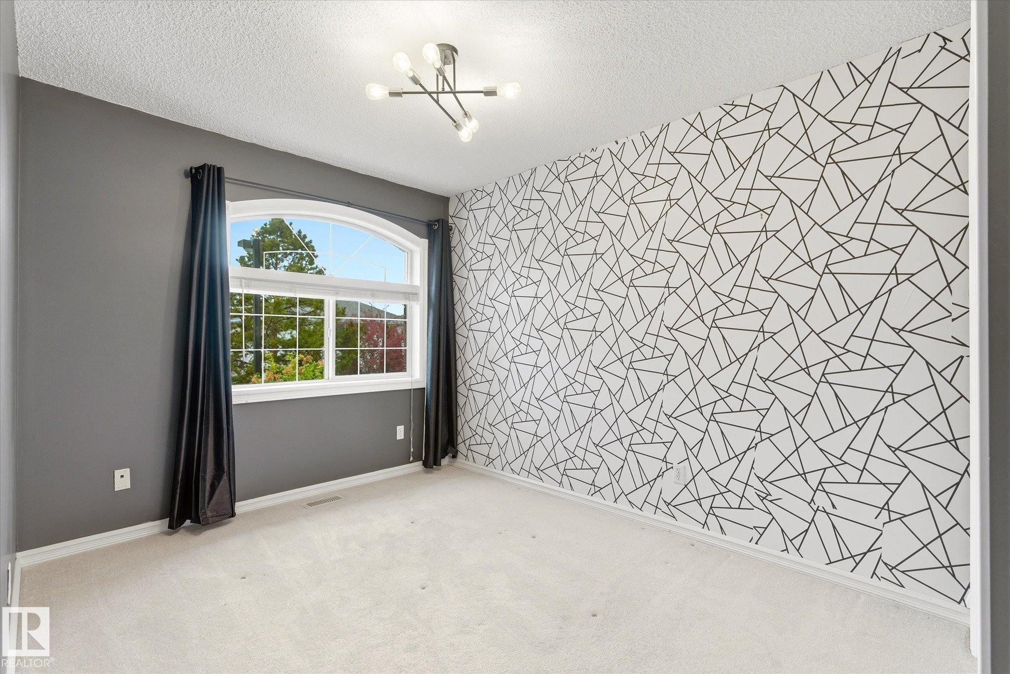 Arched window with gridded panes, modern ceiling light fixture, textured accent wall, and light-colored carpeting - 2550 Rabbit Hill Road Nw, Edmonton, AB