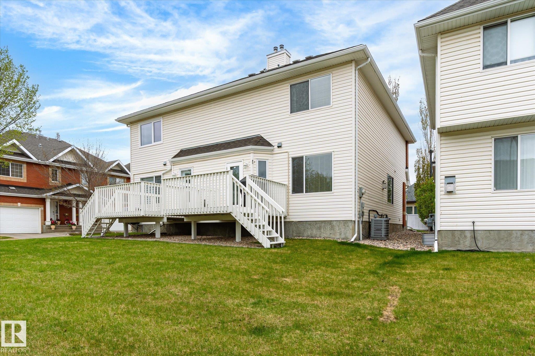 Expansive rear yard featuring a large elevated deck with railings and staircase, light-colored siding, and a prominent bay window - 2550 Rabbit Hill Road Nw, Edmonton, AB