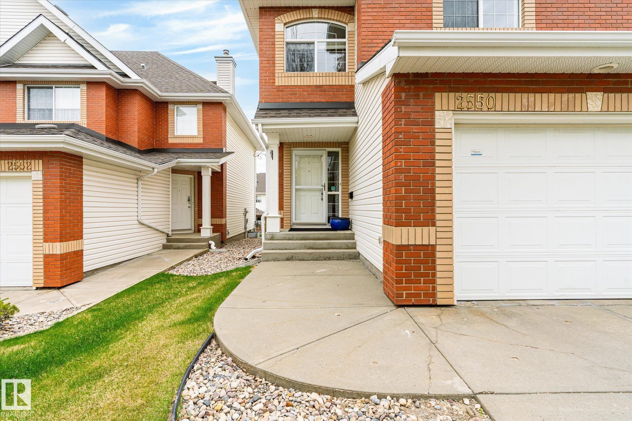 Brick and siding exterior with arched window detail, integrated garage, and concrete walkway - 2550 Rabbit Hill Road Nw, Edmonton, AB