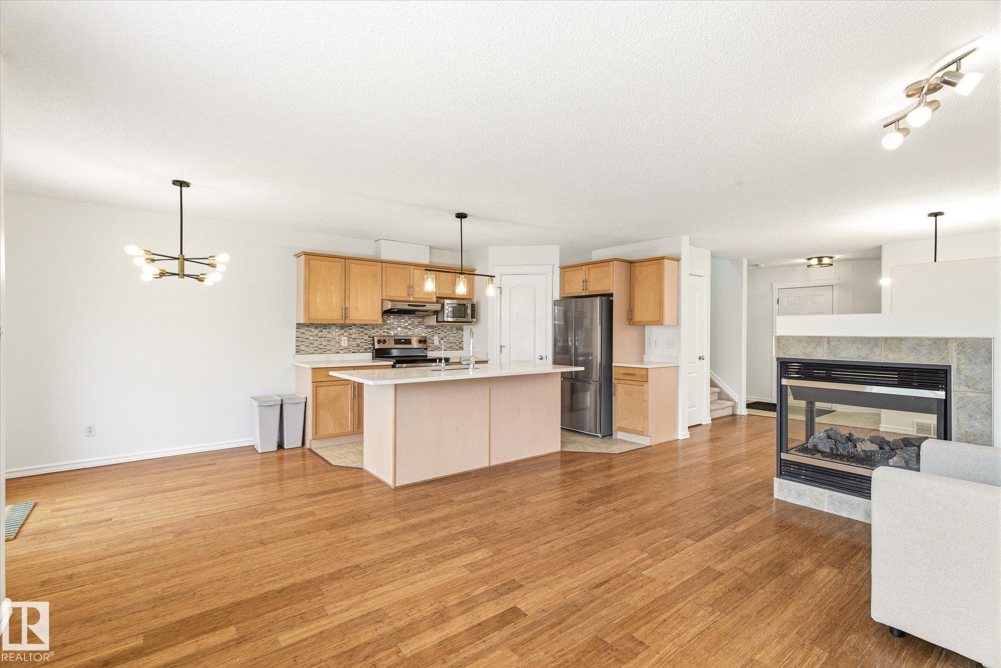 Open concept living area featuring wood-finish flooring, a kitchen island, light wood cabinetry, and a fireplace with a stone surround - 2550 Rabbit Hill Road Nw, Edmonton, AB