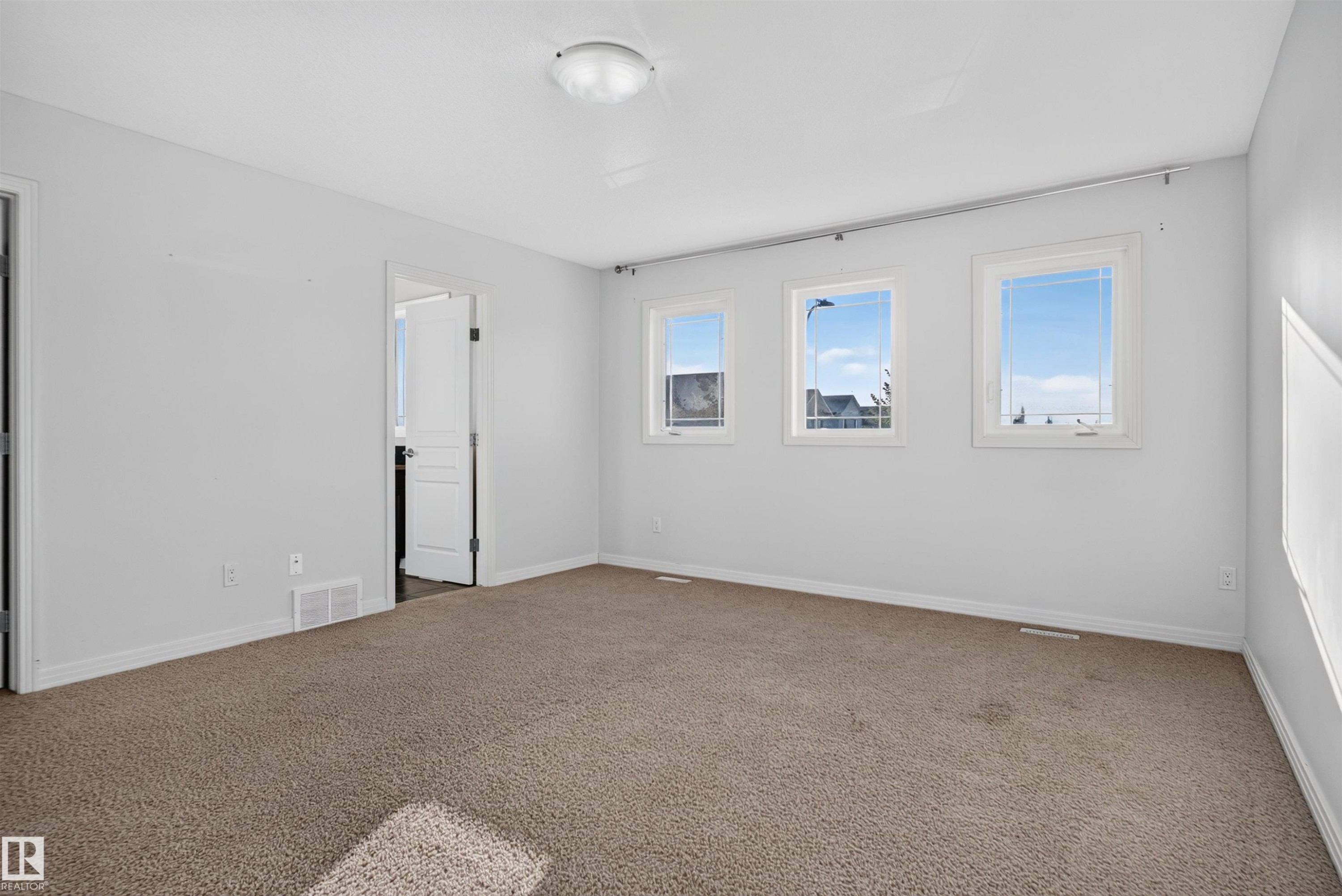 Carpeted room featuring multiple windows, a ceiling-mounted light fixture, and white trim - 2145 28 Street Nw, Edmonton, AB