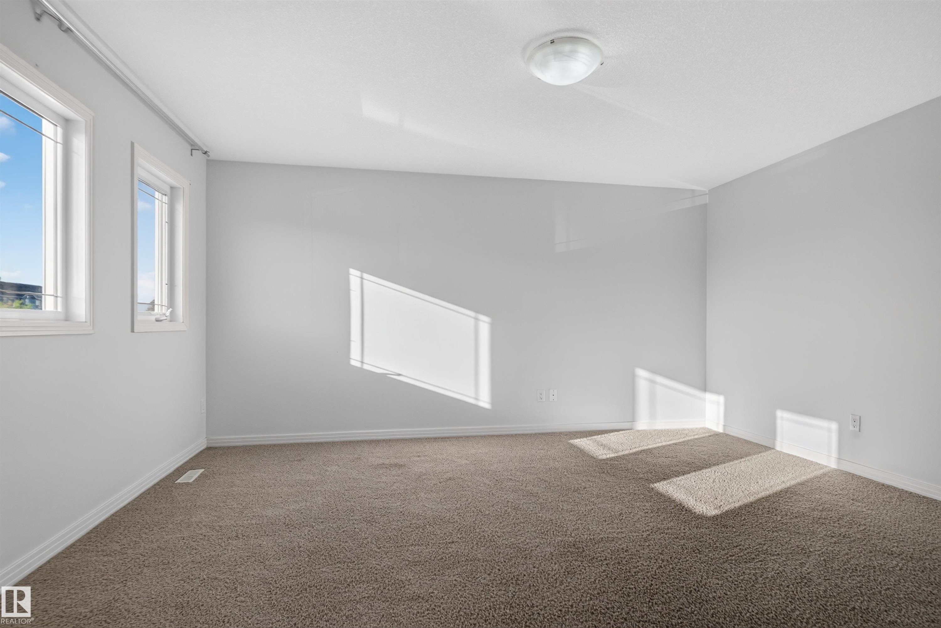 Expansive room with neutral carpeting, light-toned walls, and multiple windows - 2145 28 Street Nw, Edmonton, AB