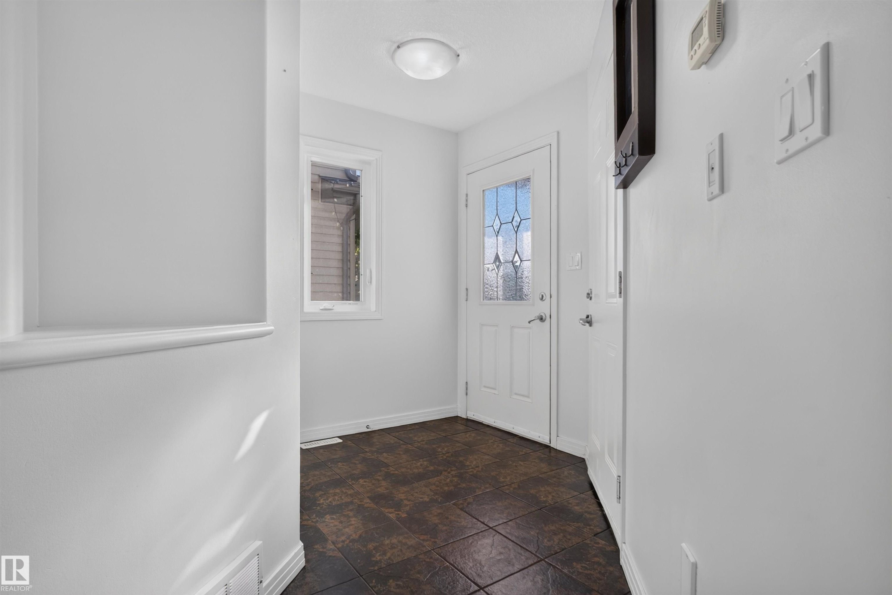 Tile flooring, white trim, white interior door with decorative glass, flush mount ceiling light, and a white framed window - 2145 28 Street Nw, Edmonton, AB