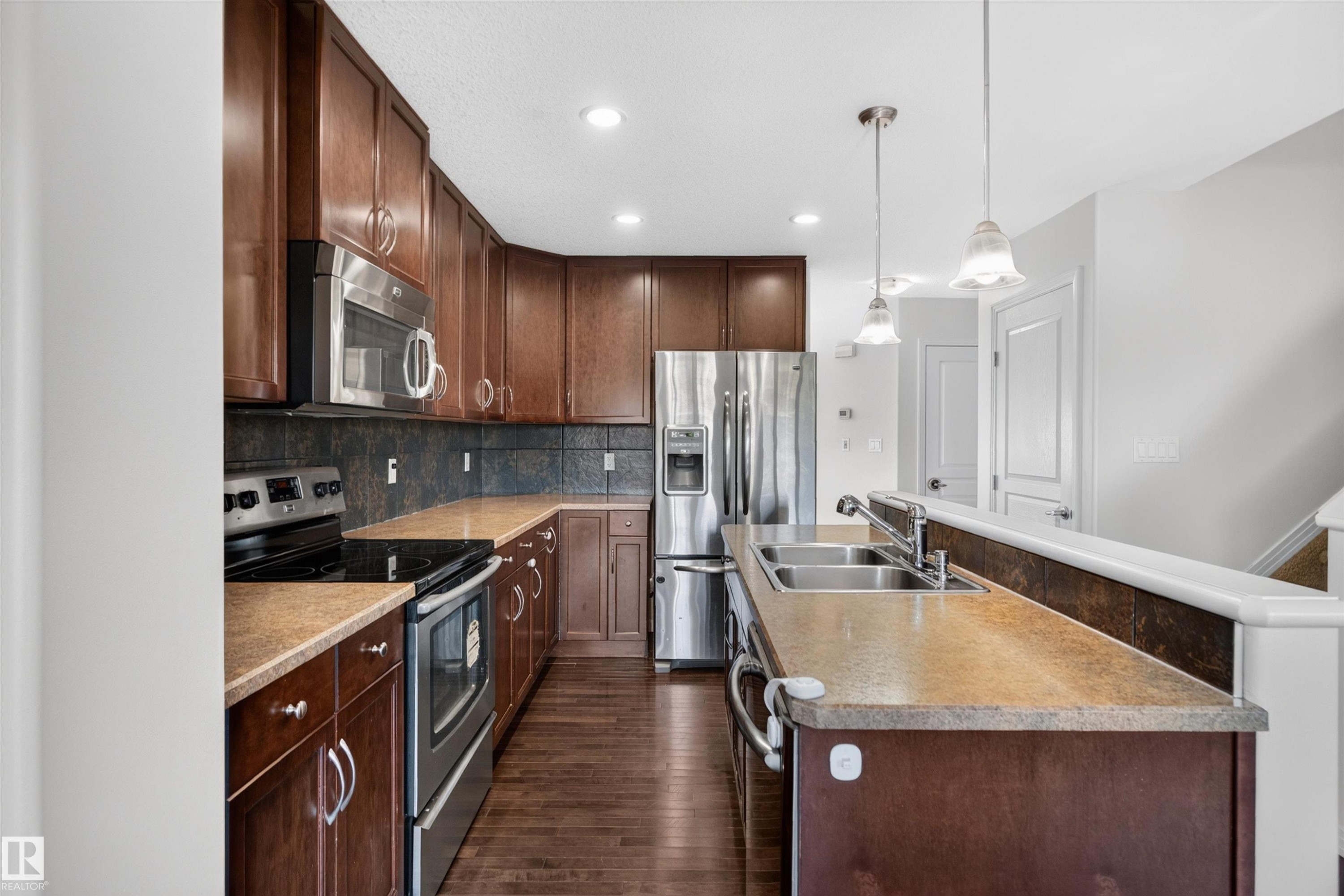 Kitchen with wood-finish flooring, stainless steel appliances, dark wood cabinetry, and a double basin sink - 2145 28 Street Nw, Edmonton, AB