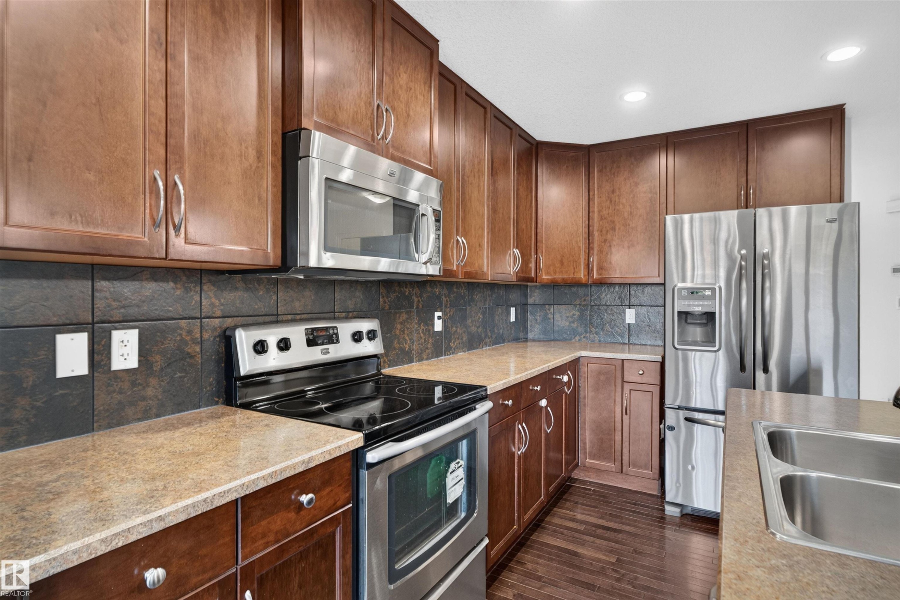 Wood-finish cabinetry with stainless steel appliances, durable countertops, dark tile backsplash, and recessed lighting - 2145 28 Street Nw, Edmonton, AB