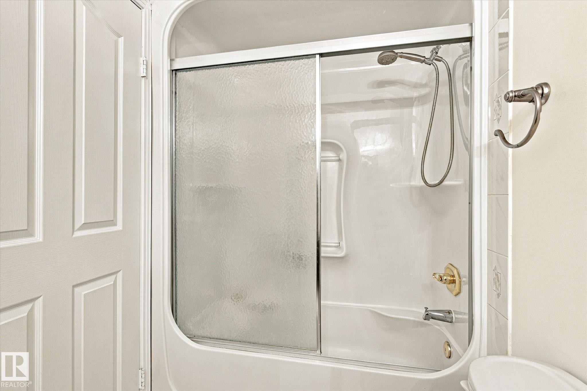 Tub and shower combination with sliding textured glass doors, polished chrome shower head, and brass-finish fixtures - 771 Johns Road Nw, Edmonton, AB