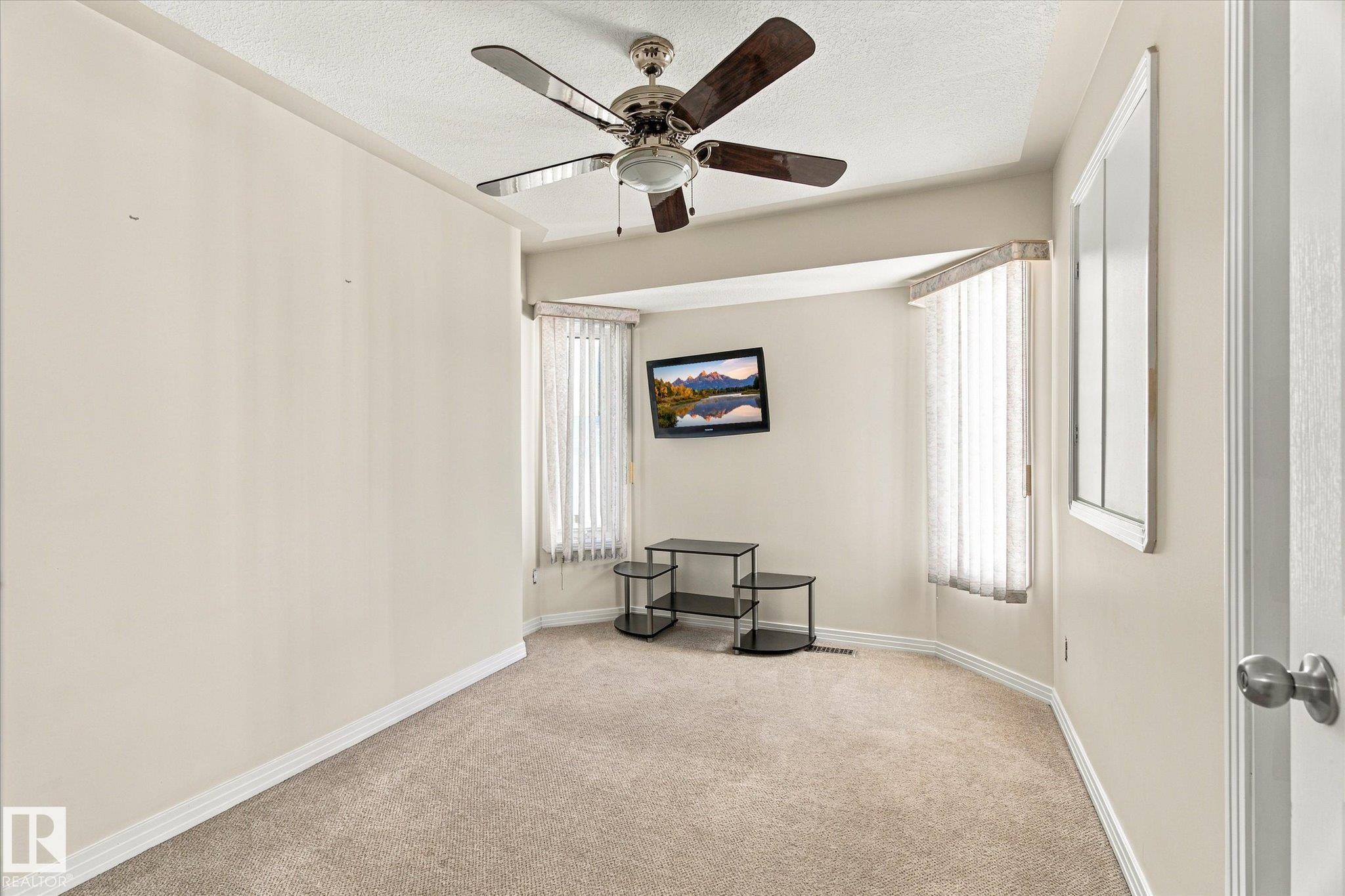 Tray ceiling with a ceiling fan, bay window with vertical blinds, and neutral carpeting - 771 Johns Road Nw, Edmonton, AB
