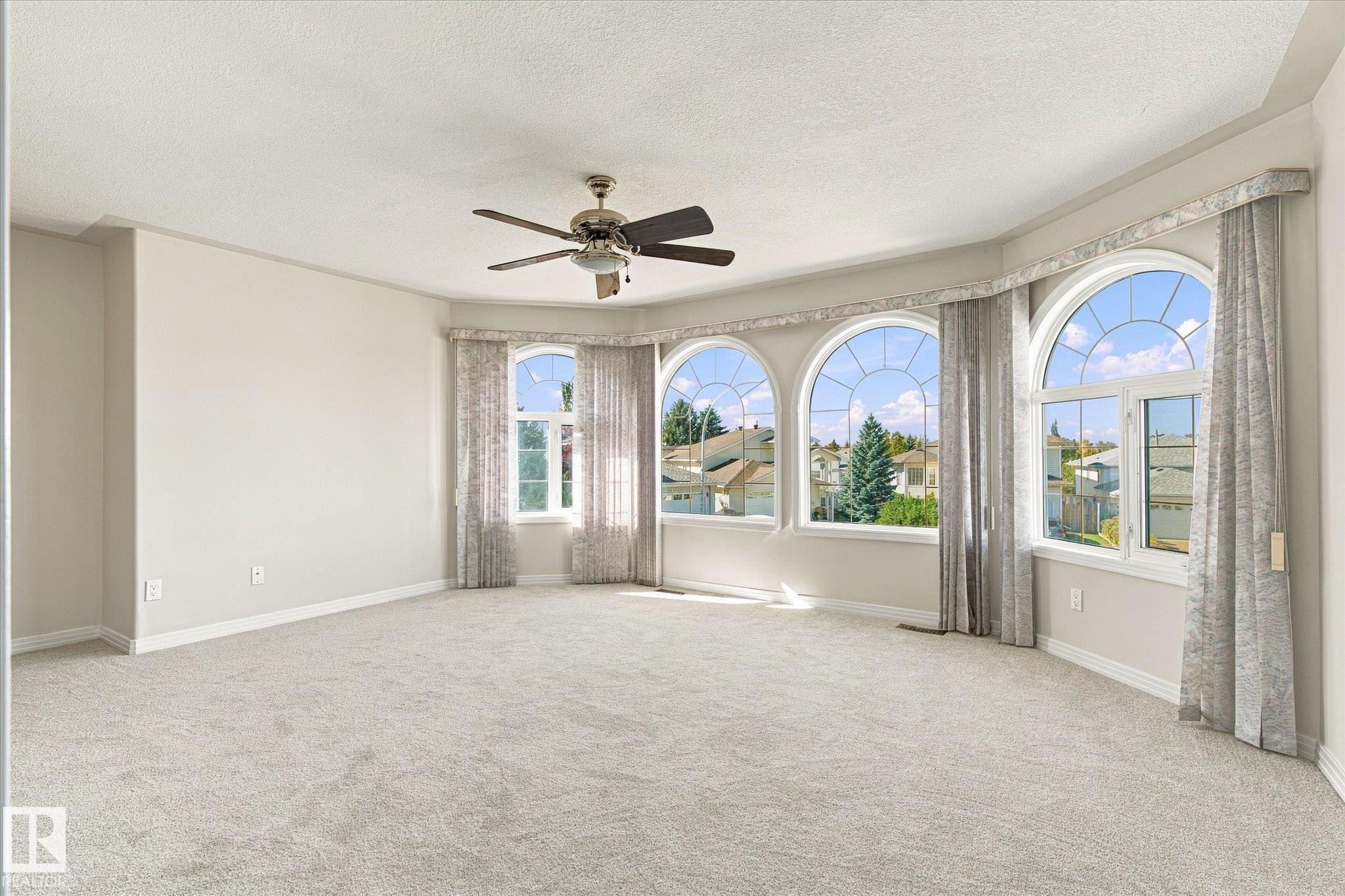 Soft neutral carpeting, a ceiling fan fixture, and a series of arched windows - 771 Johns Road Nw, Edmonton, AB