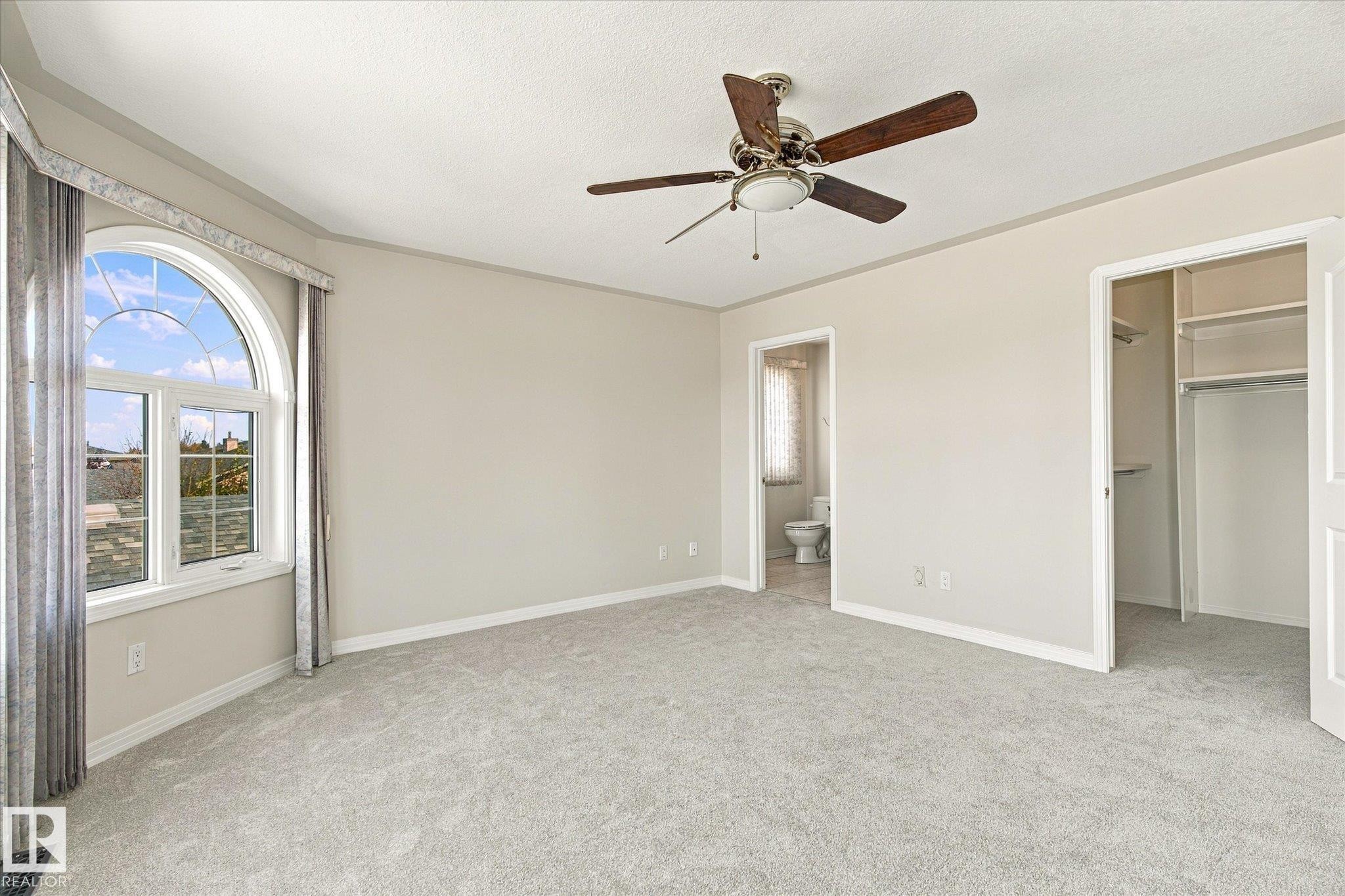 Arched window with upper transom, wall-to-wall carpeting, ceiling fan with integrated lighting, built-in closet shelving, and a permanent door leading to a separate area - 771 Johns Road Nw, Edmonton, AB