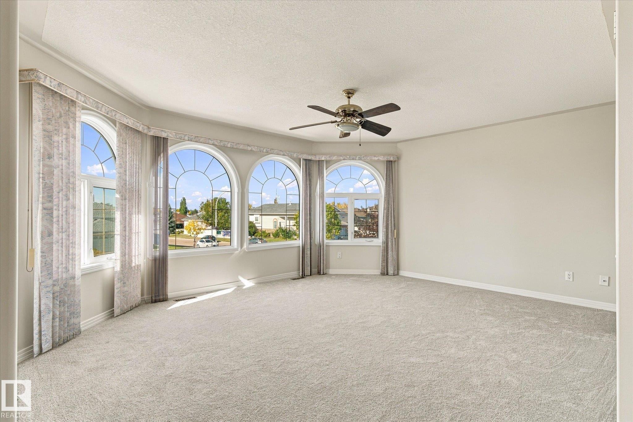 Expansive room featuring a bay of arched windows, light-toned wall finishes, and a ceiling fan with integrated lighting - 771 Johns Road Nw, Edmonton, AB
