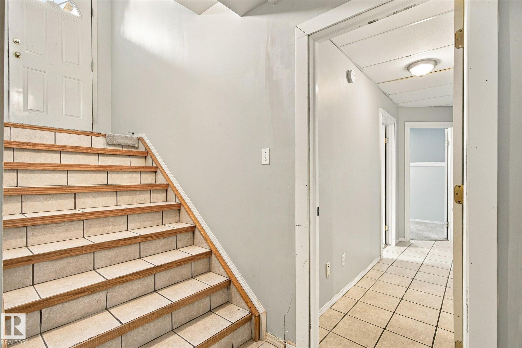 Tiled staircase with wood-finish trim, leading to a white paneled door - 771 Johns Road Nw, Edmonton, AB