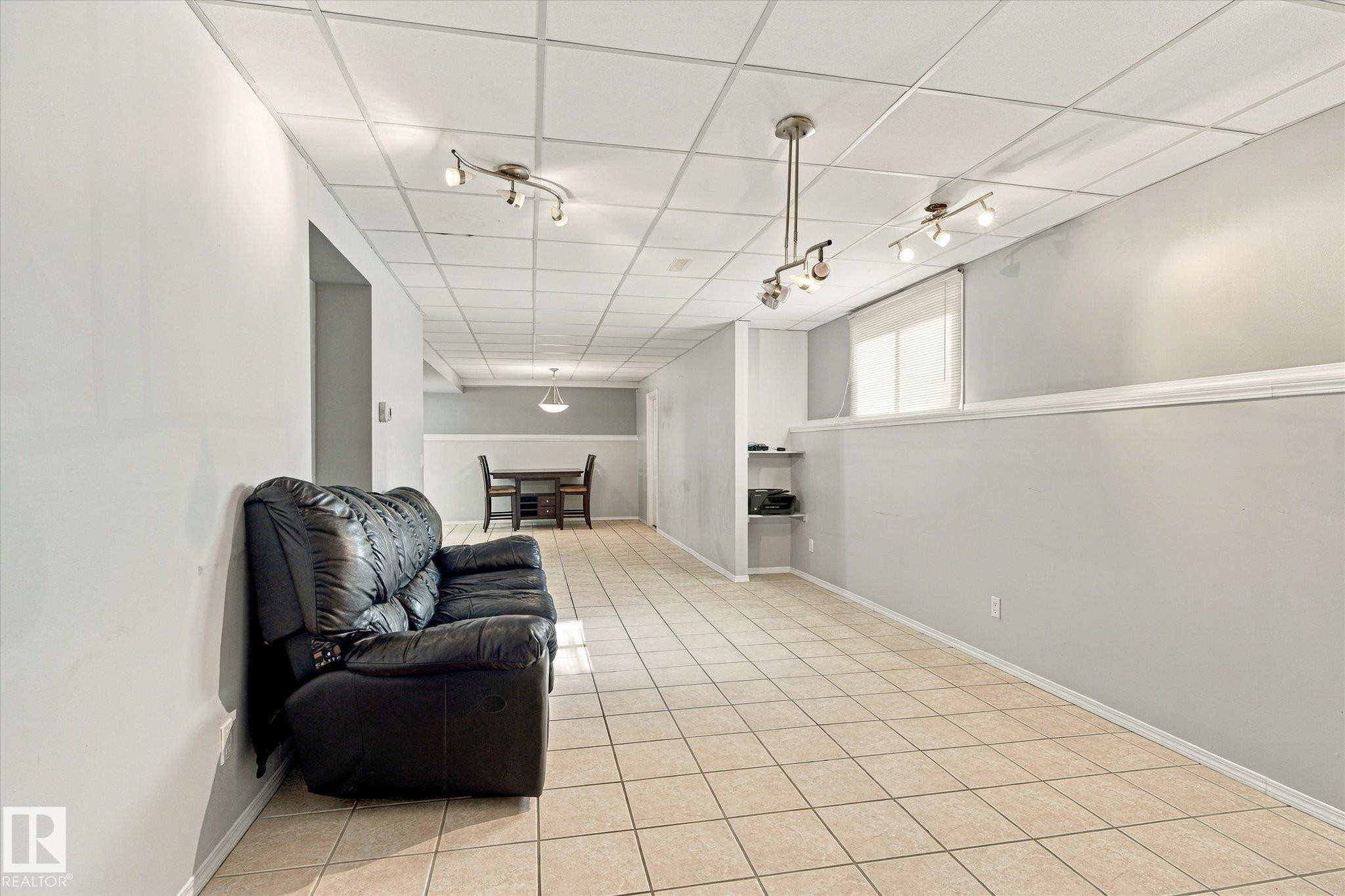 Expansive room featuring light-colored tile flooring, drop ceiling panels, recessed shelving, and multiple track lighting fixtures - 771 Johns Road Nw, Edmonton, AB