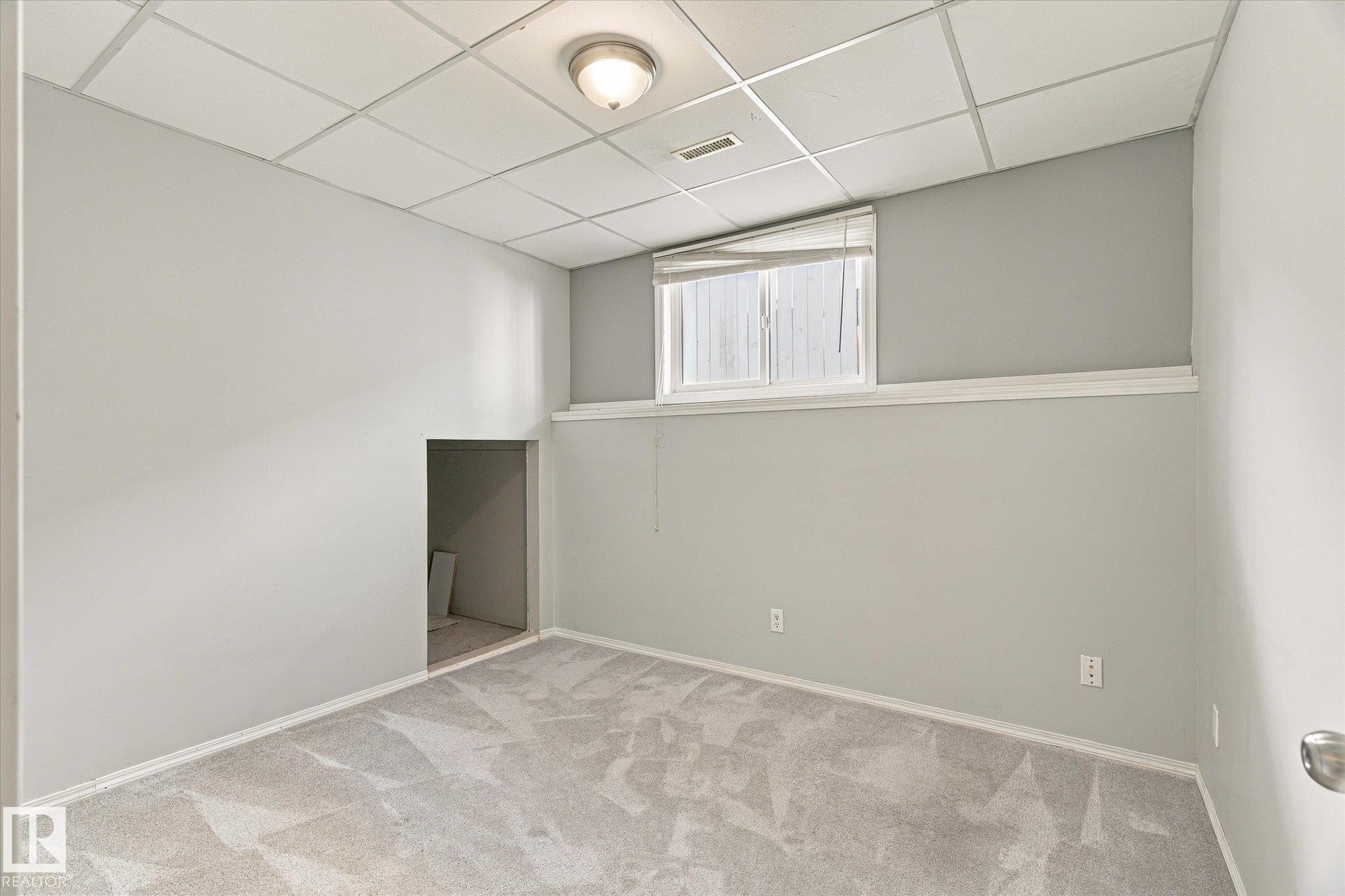 Wall-to-wall carpeting with a light pattern, drop ceiling with recessed lighting, painted walls, and a window with blinds - 771 Johns Road Nw, Edmonton, AB
