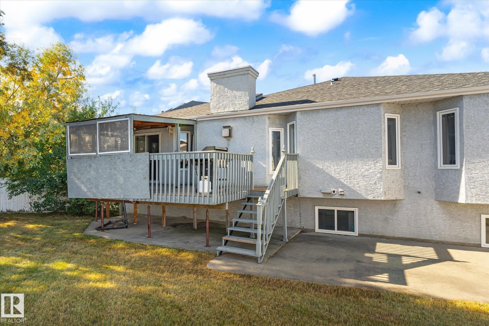 Exterior featuring a screened-in porch, wooden deck, stairs to ground level, stucco siding, and multiple windows - 771 Johns Road Nw, Edmonton, AB