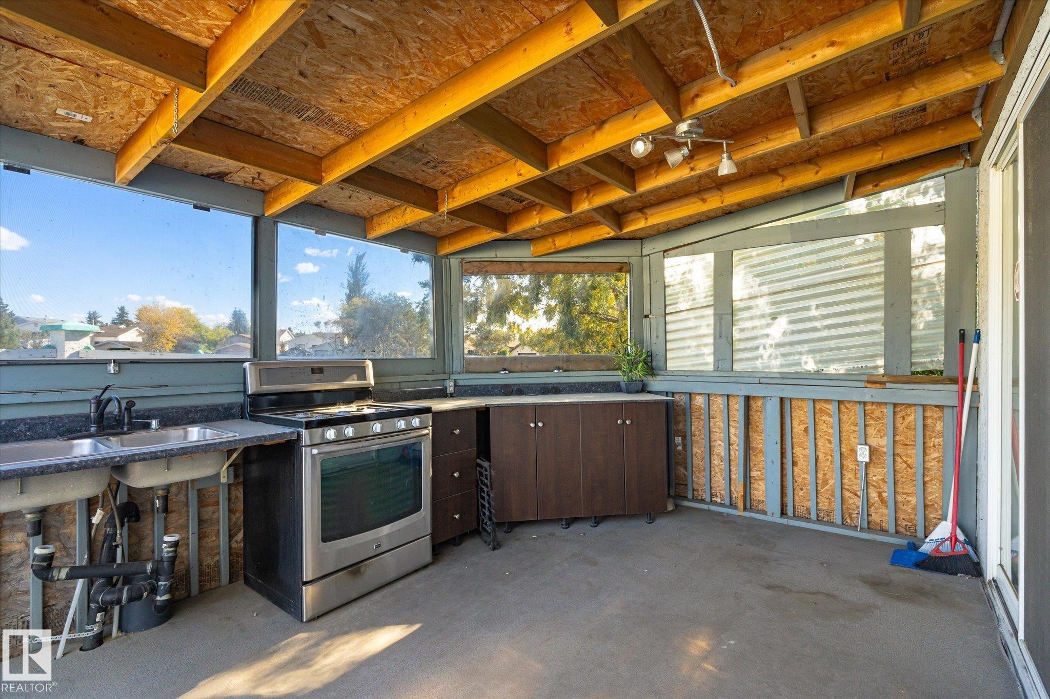 Enclosed outdoor space featuring an exposed wood beam ceiling, concrete flooring, stainless steel range, double basin sink, and dark cabinetry - 771 Johns Road Nw, Edmonton, AB