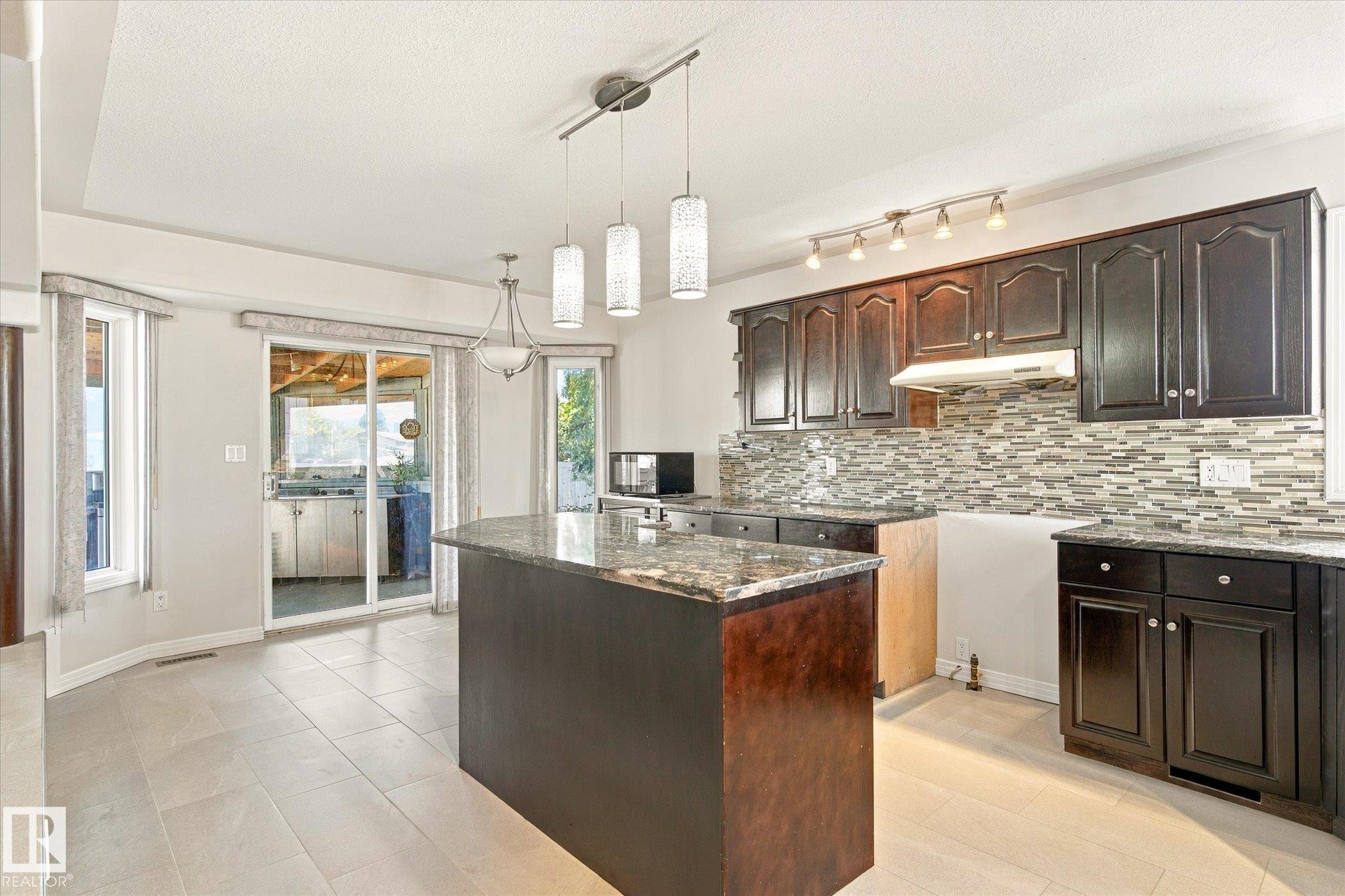 Kitchen featuring dark wood cabinetry, a granite-finish island, and a mosaic tile backsplash - 771 Johns Road Nw, Edmonton, AB
