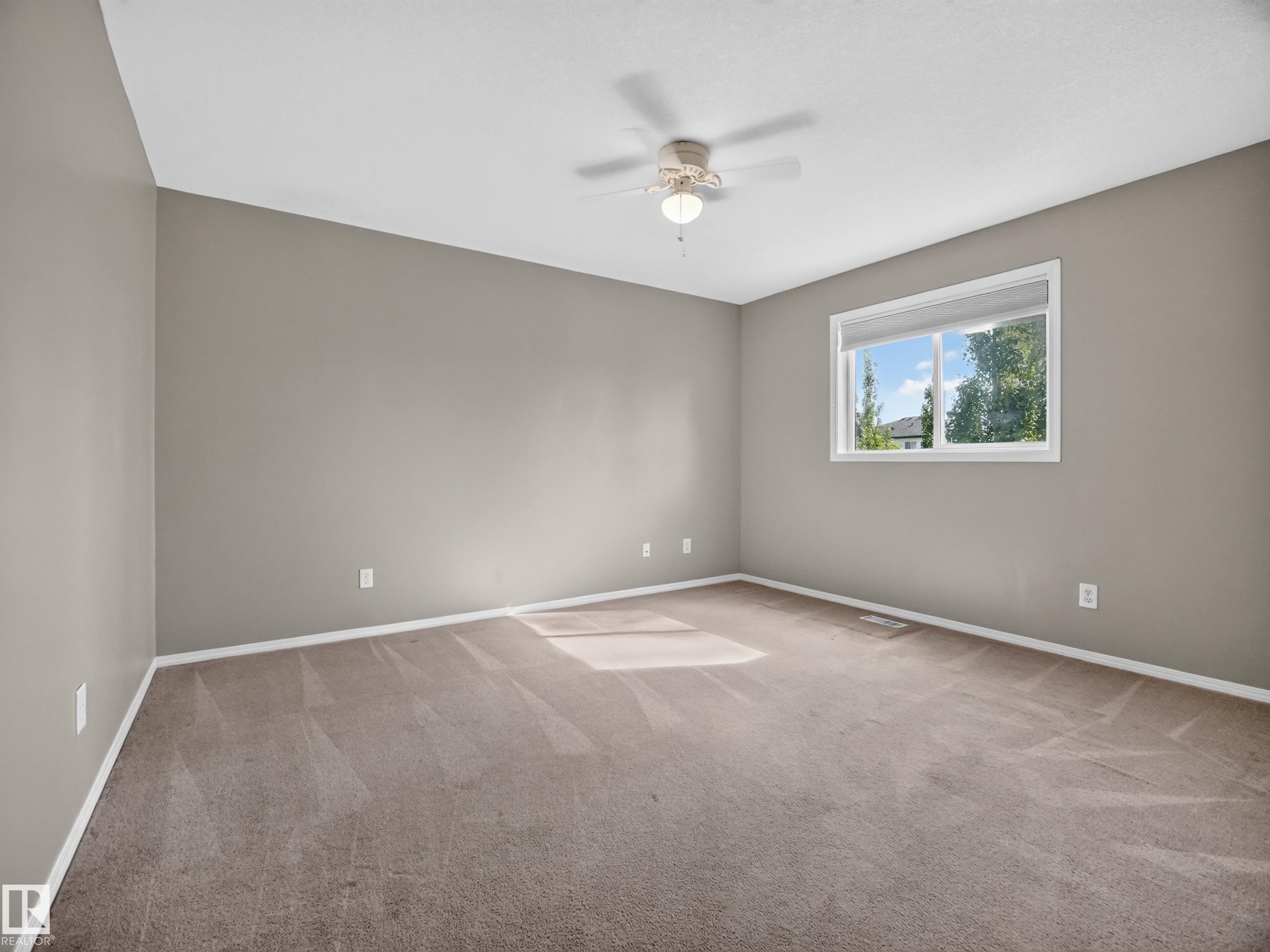 Neutral-toned walls with a white-framed window, overhead ceiling fan with lighting, and plush carpeting - 14 Wells Court, Leduc, AB