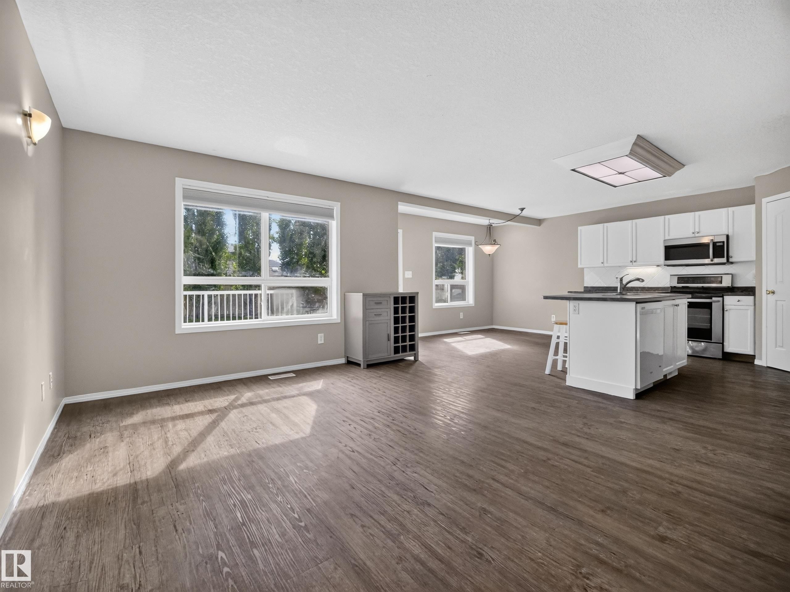 Open-concept living space featuring wood-finish flooring, white cabinetry, stainless steel appliances, and a kitchen island with a breakfast bar - 14 Wells Court, Leduc, AB