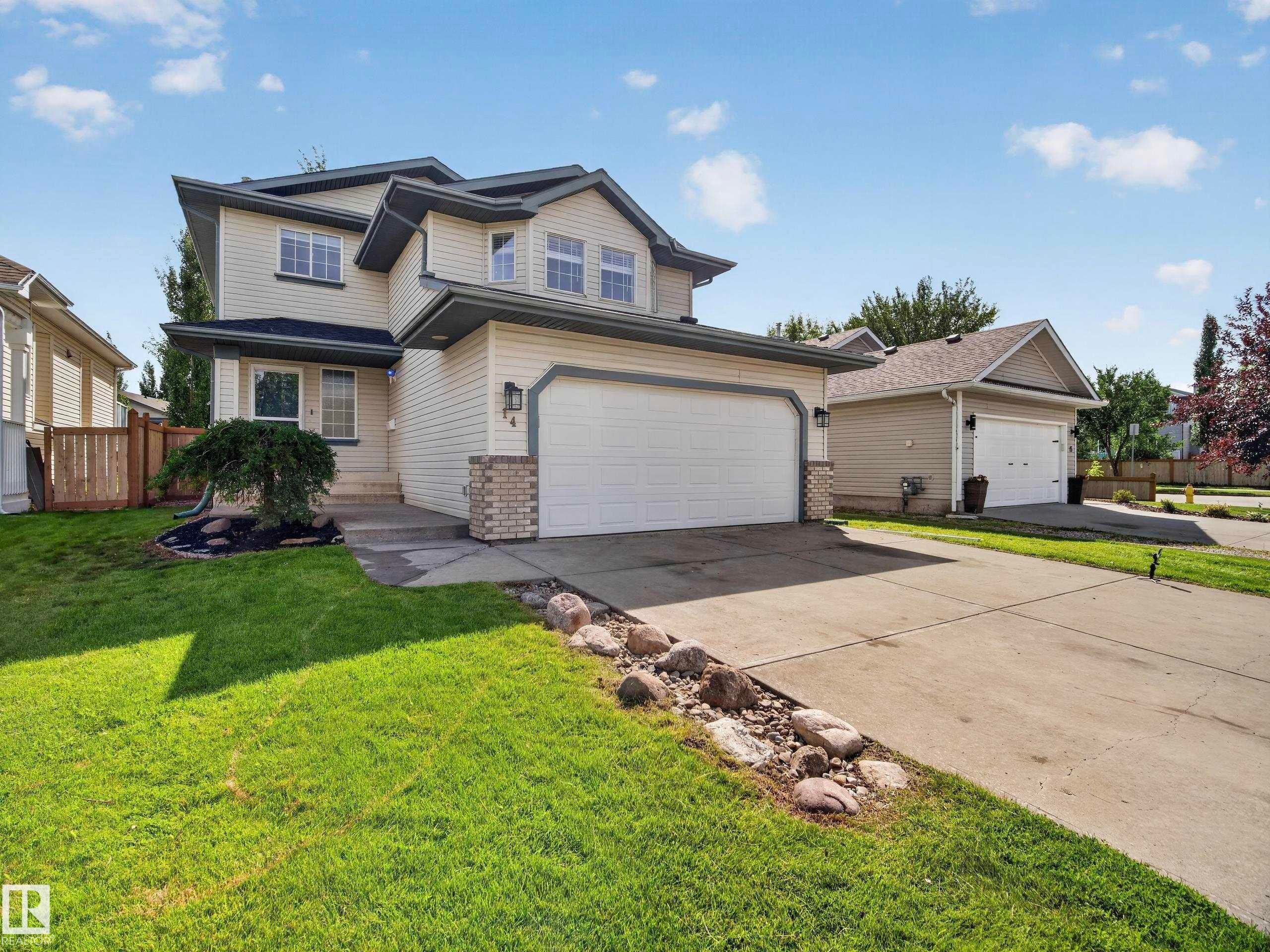 Two-story exterior with light-toned siding, attached two-car garage, concrete driveway, and a manicured lawn - 14 Wells Court, Leduc, AB
