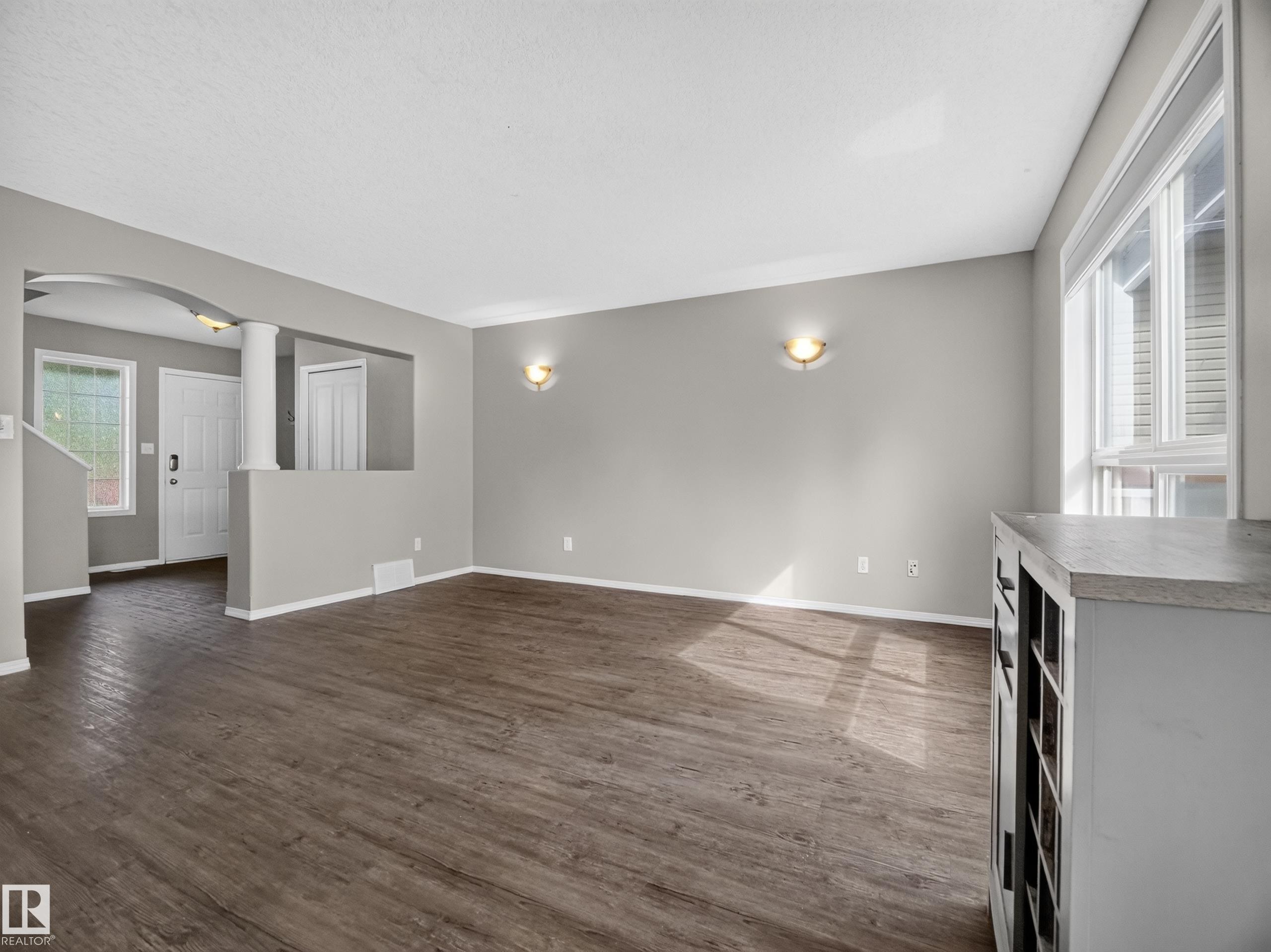 Spacious main living area featuring wood-finish flooring, neutral paint palette, ample natural light from large windows, and an arched entry - 14 Wells Court, Leduc, AB