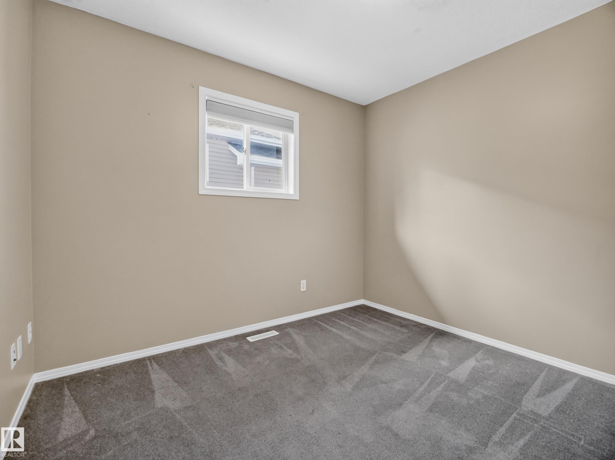 Neutral painted walls, grey carpeting, and a white framed window - 14 Wells Court, Leduc, AB