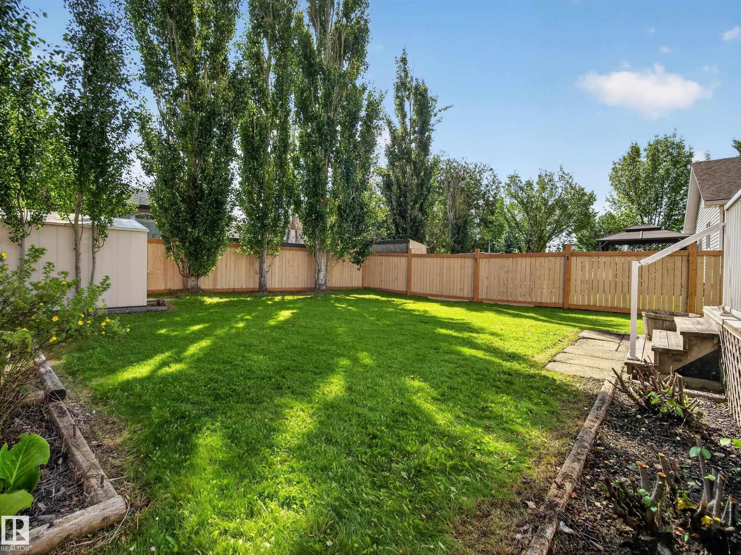 Expansive grass lawn bordered by a wood privacy fence and mature trees - 14 Wells Court, Leduc, AB
