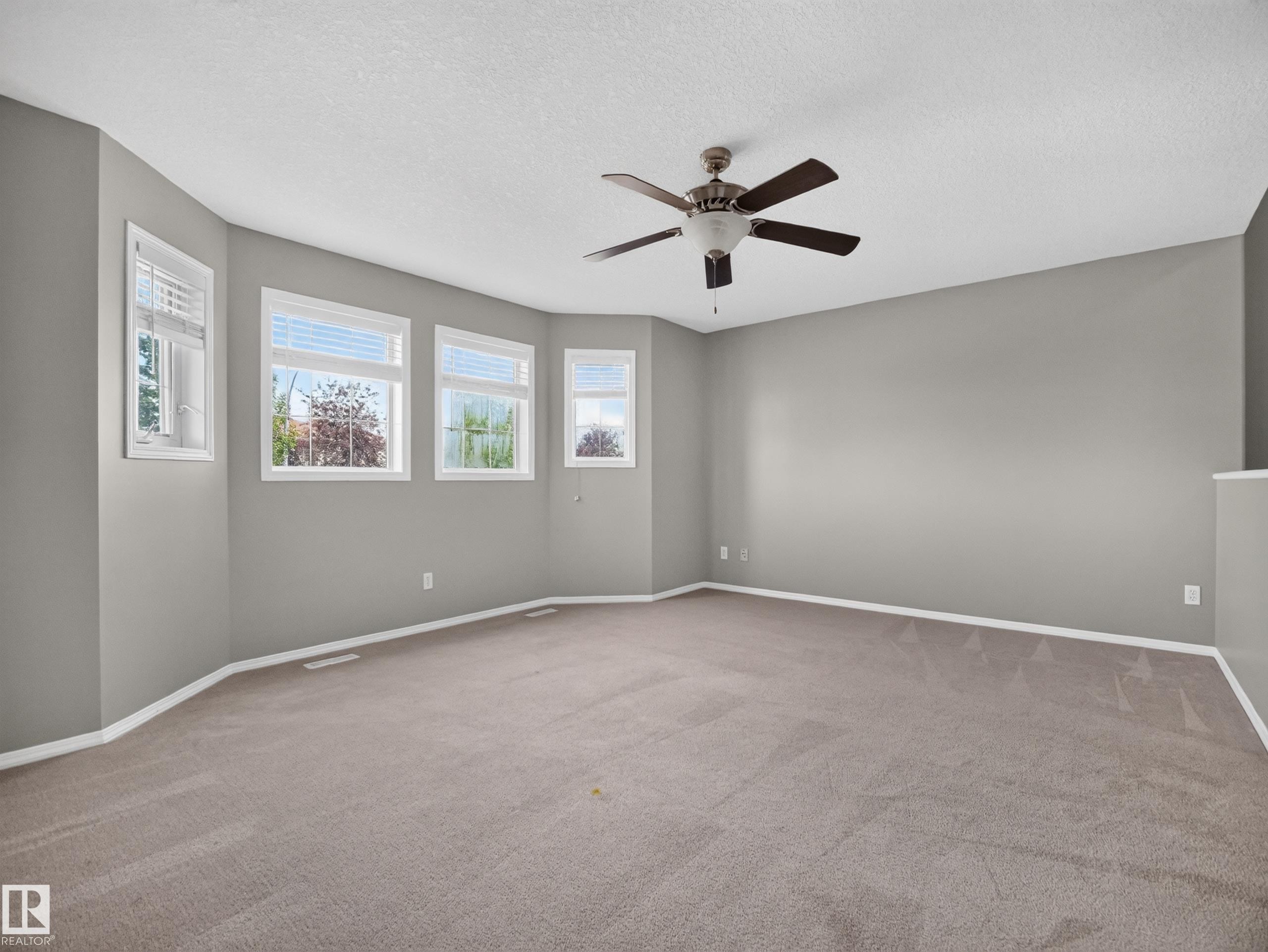 Spacious room with multiple windows, neutral carpeting, and a ceiling fan - 14 Wells Court, Leduc, AB