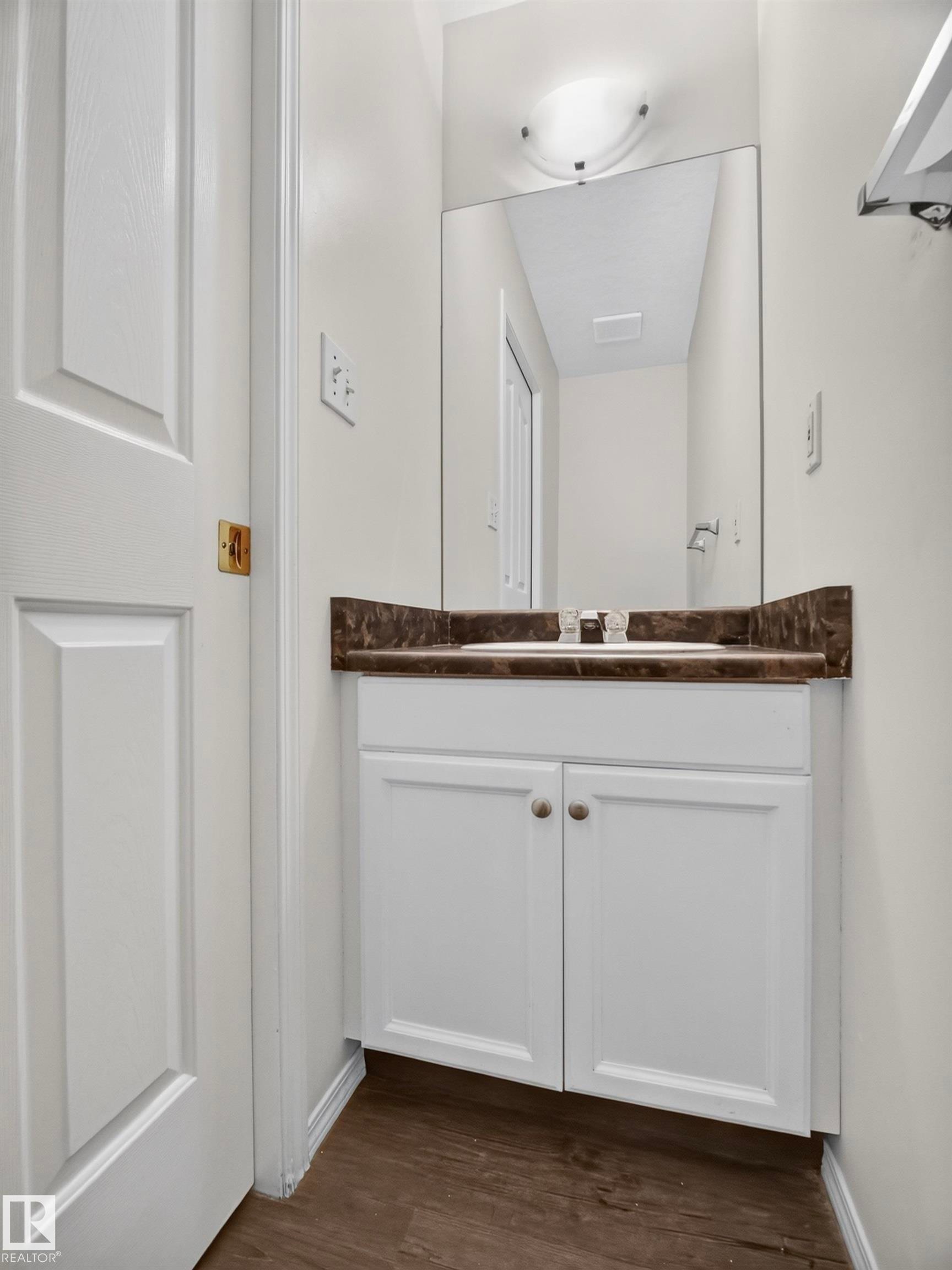 White vanity cabinetry with a dark stone-finish countertop, undermount sink, and wood-finish flooring - 14 Wells Court, Leduc, AB
