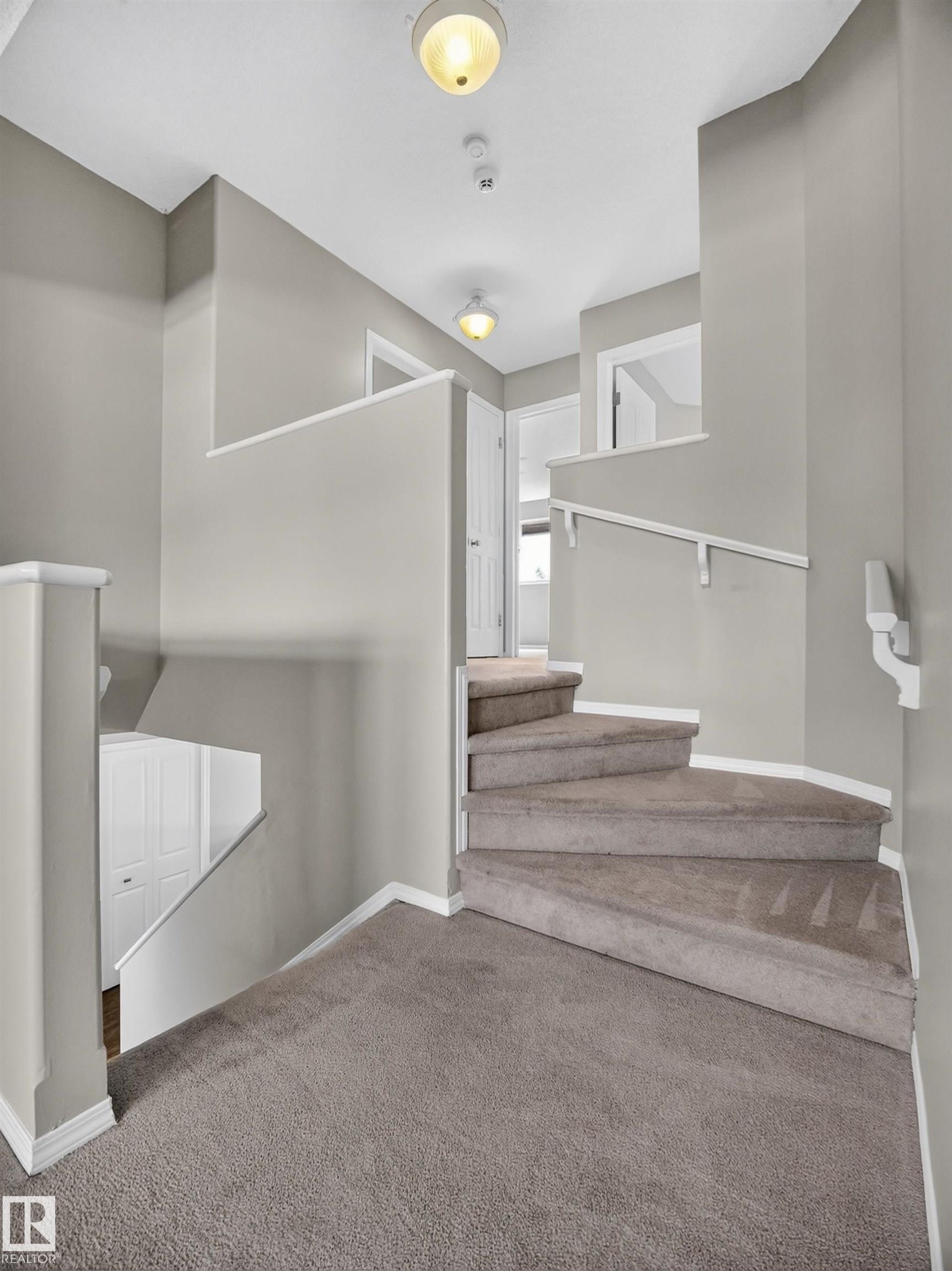 Carpeted staircase with white handrails and neutral wall paint - 14 Wells Court, Leduc, AB