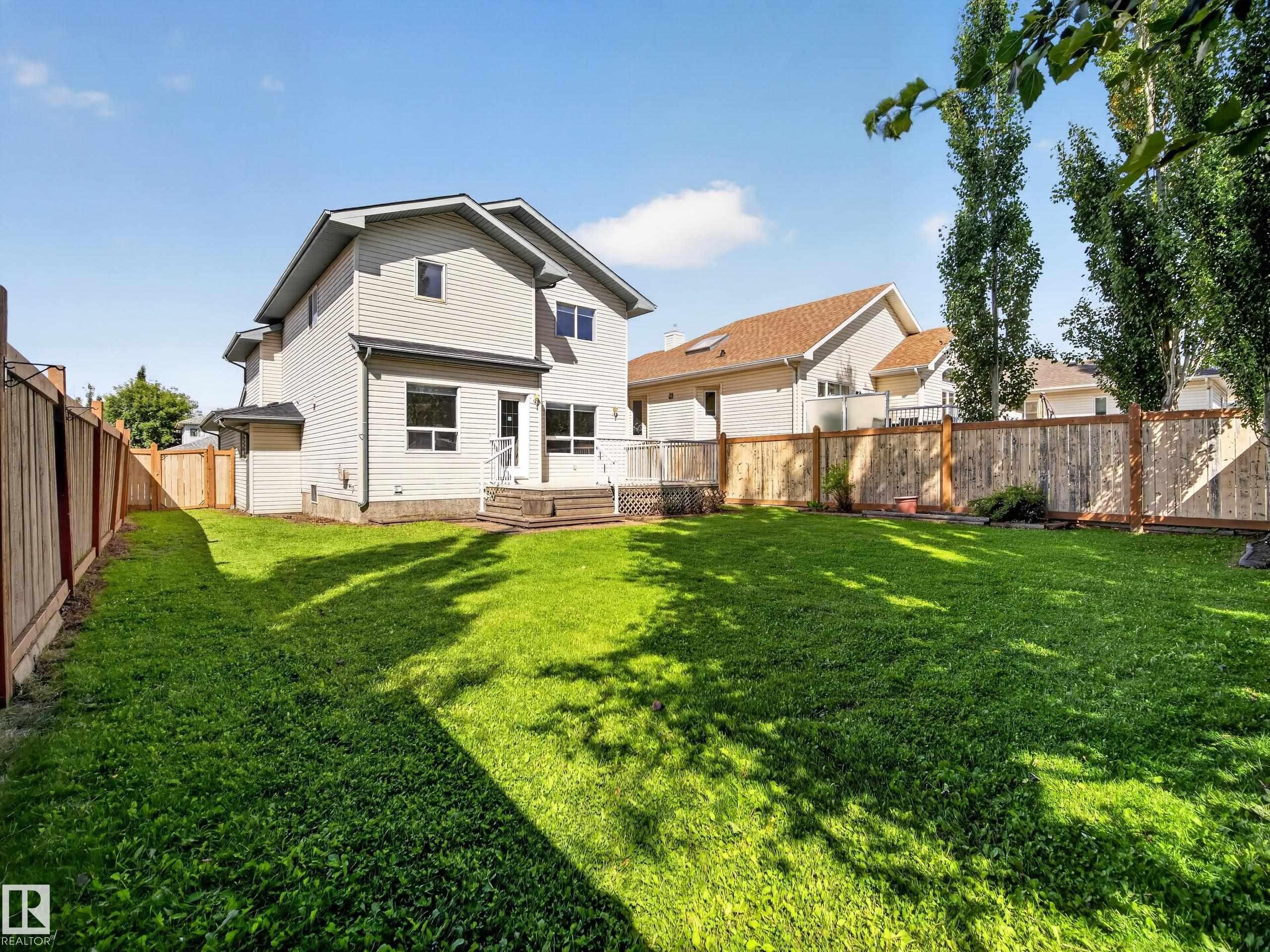 Expansive backyard featuring a manicured lawn, wood fencing, and a multi-level deck - 14 Wells Court, Leduc, AB