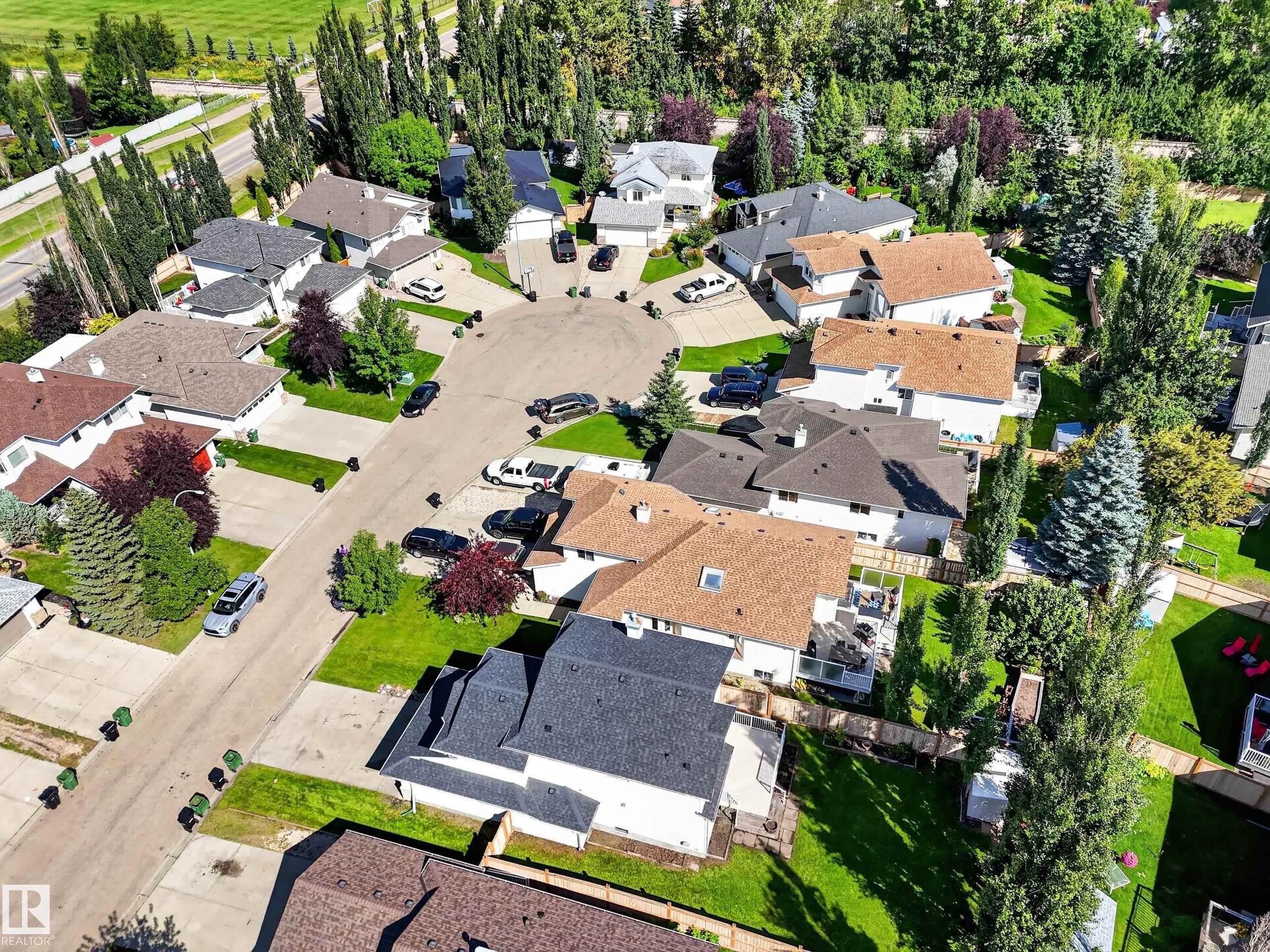 Residential properties featuring various roof styles, mature trees, and landscaped yards - 14 Wells Court, Leduc, AB
