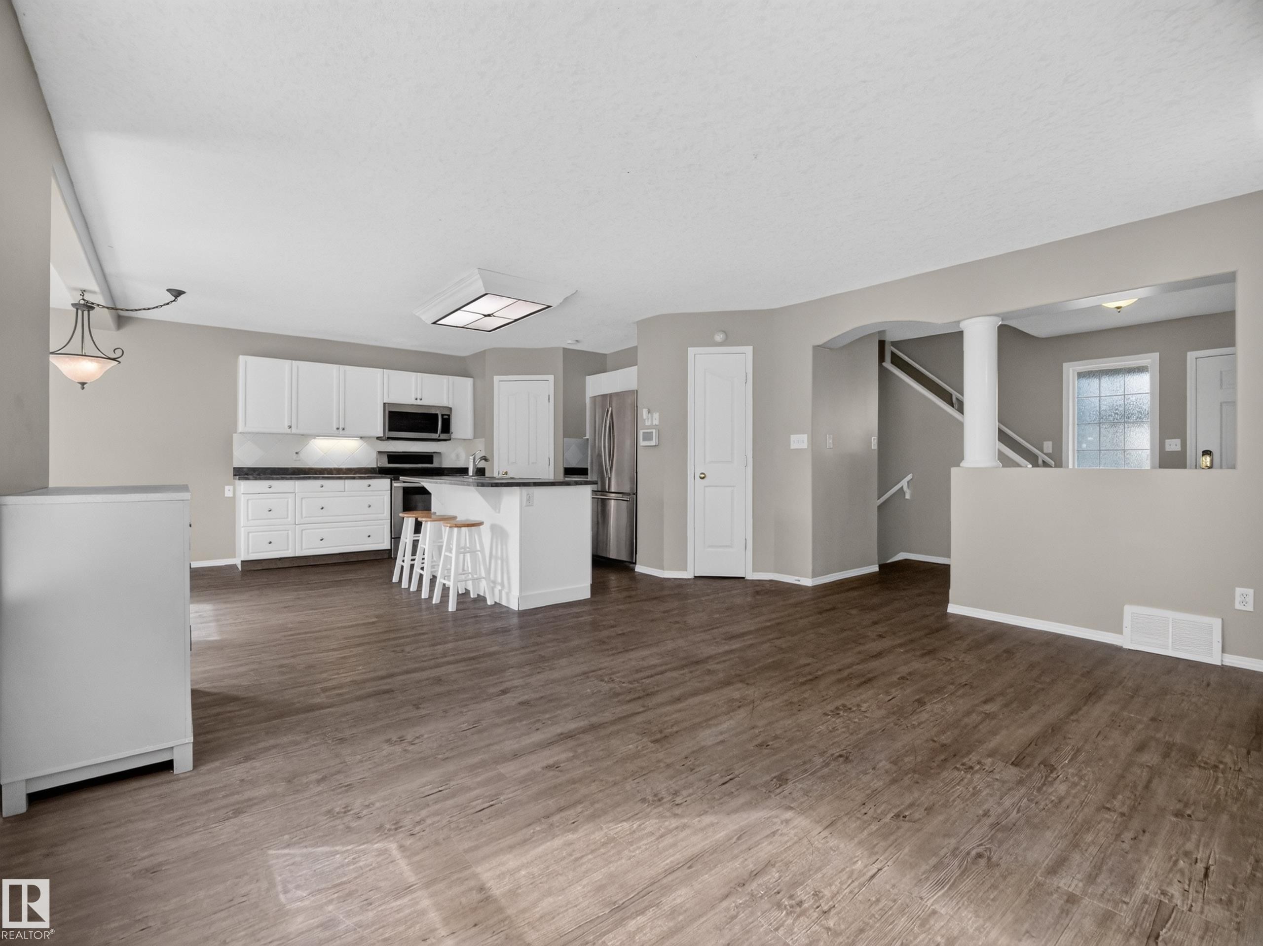 Open-concept living space with wood-finish flooring, white cabinetry, a kitchen island, and stainless steel appliances - 14 Wells Court, Leduc, AB