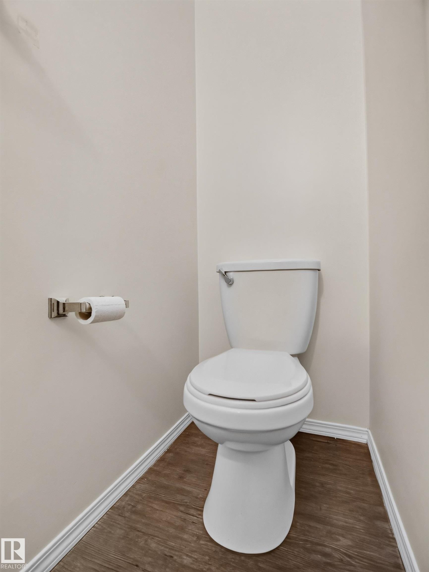 Wood-finish flooring with white trim, a white toilet, and a brushed nickel toilet paper holder - 14 Wells Court, Leduc, AB