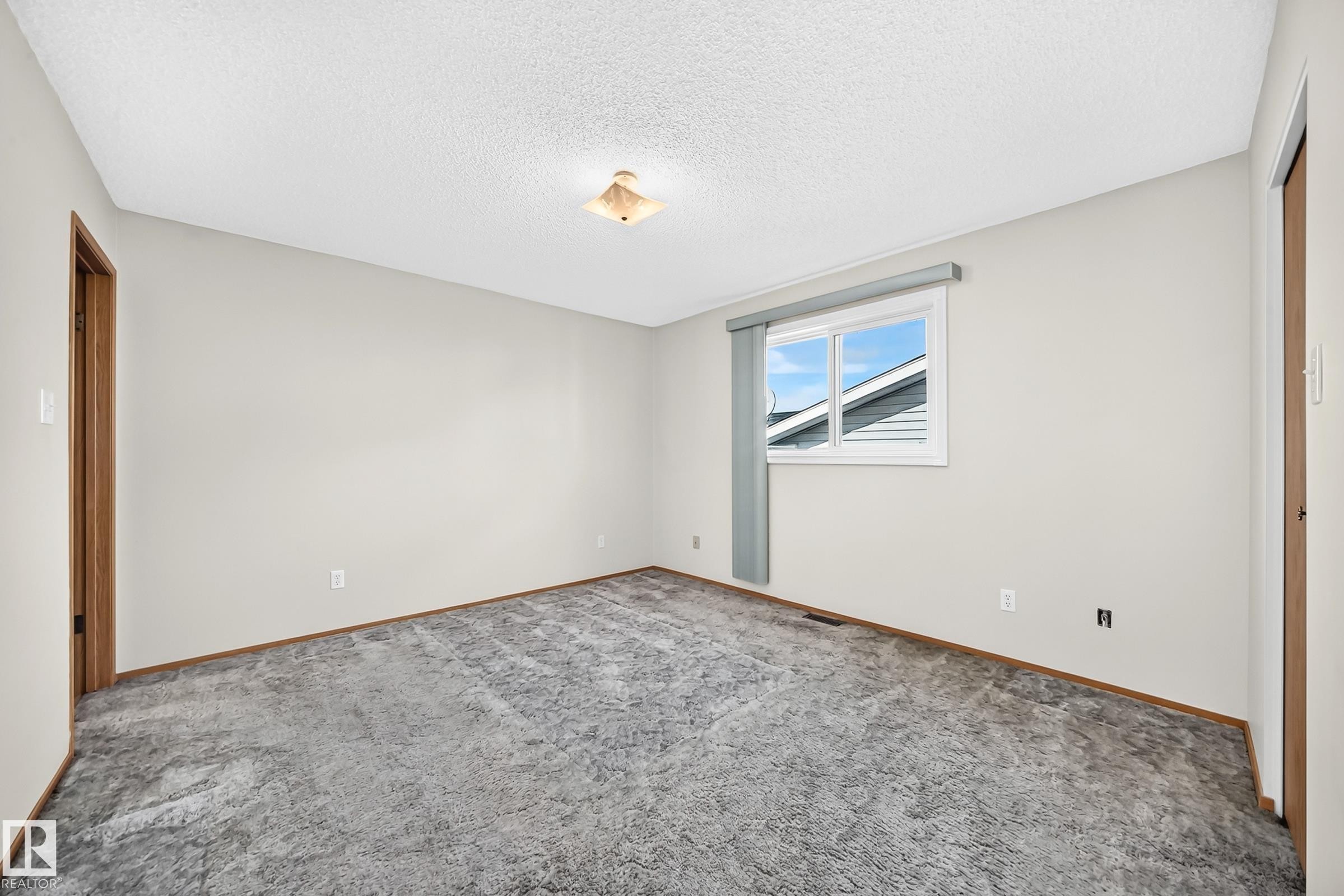 Neutral wall color, wall-to-wall carpeting, wood-finish trim, flush mount ceiling light, and window - 14519 32 Street Nw, Edmonton, AB