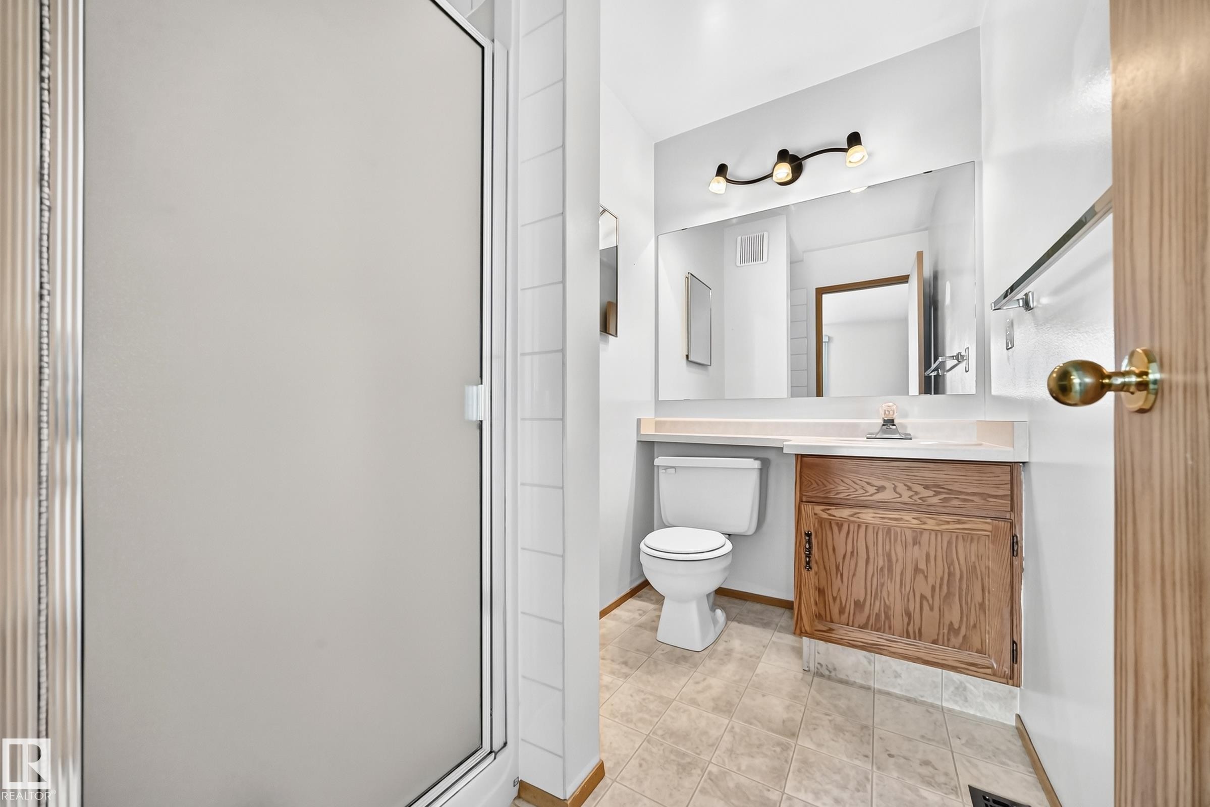 Frosted glass shower enclosure, wood-finish vanity with countertop, large wall-mounted mirror, and tile flooring - 14519 32 Street Nw, Edmonton, AB