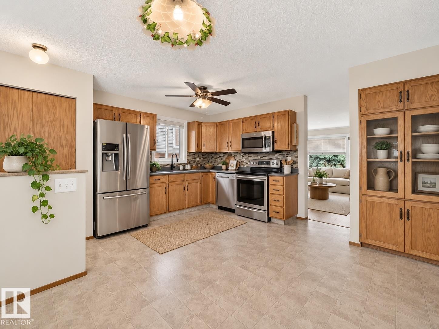 Kitchen featuring wood cabinetry, stainless steel appliances, mosaic tile backsplash, and durable tile flooring - 14519 32 Street Nw, Edmonton, AB
