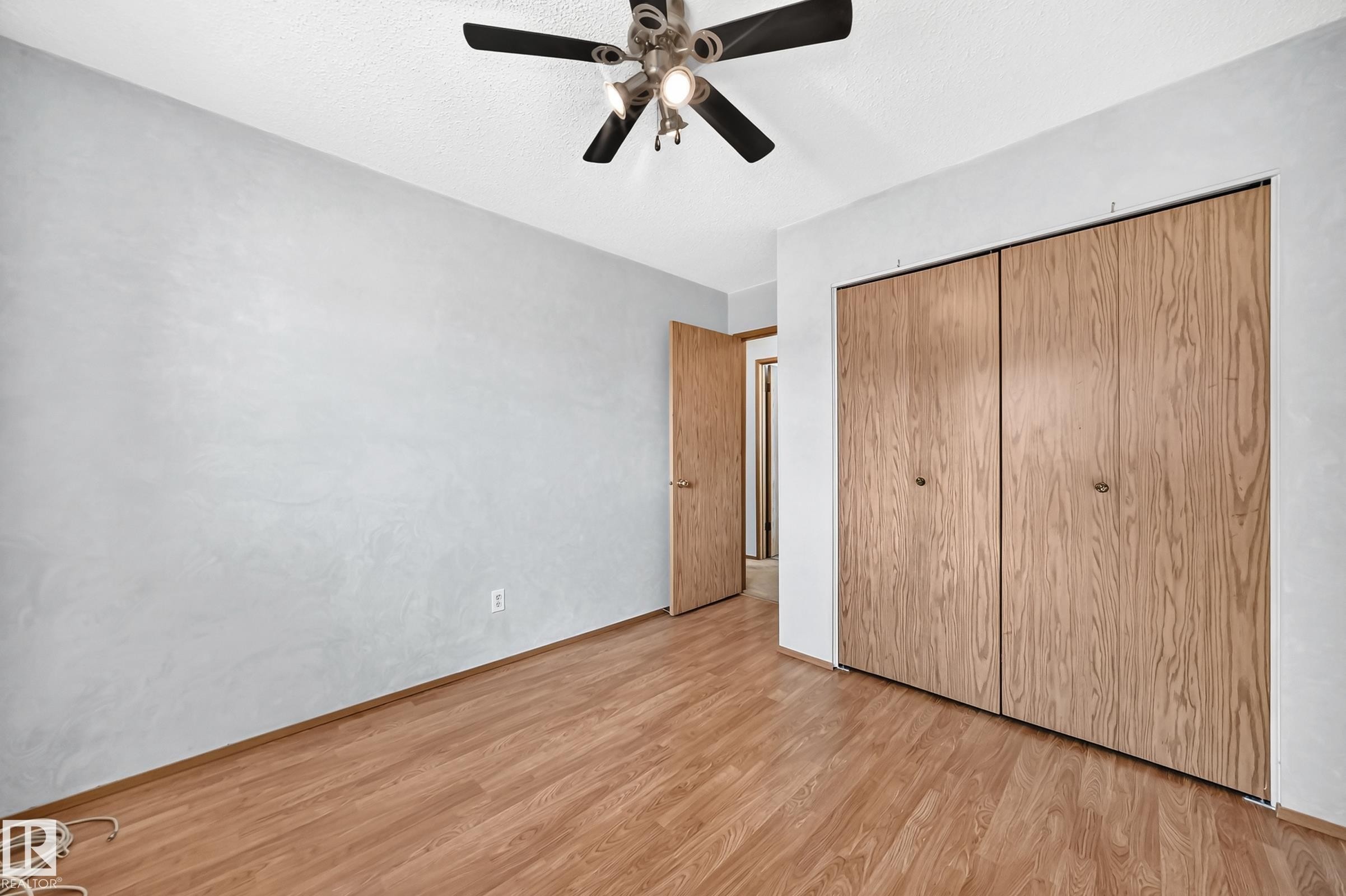 Wood-finish flooring, bi-fold closet doors, ceiling fan with integrated lighting, and a neutral wall finish - 14519 32 Street Nw, Edmonton, AB