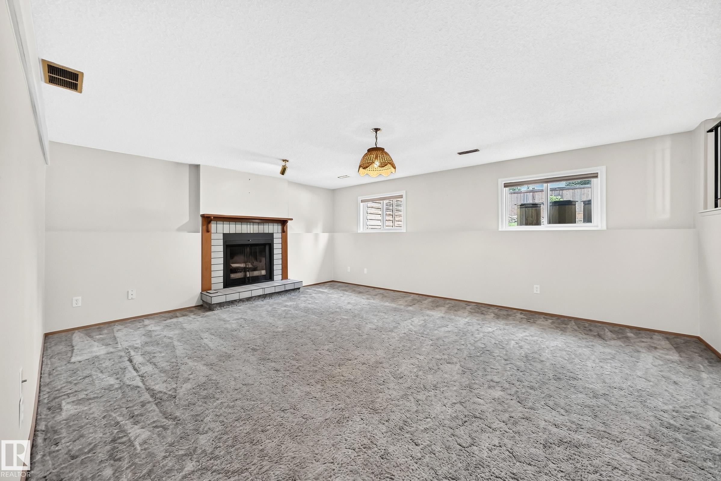 Spacious living area featuring neutral carpeting, recessed ceiling lighting, and a brick fireplace with dark surround - 14519 32 Street Nw, Edmonton, AB