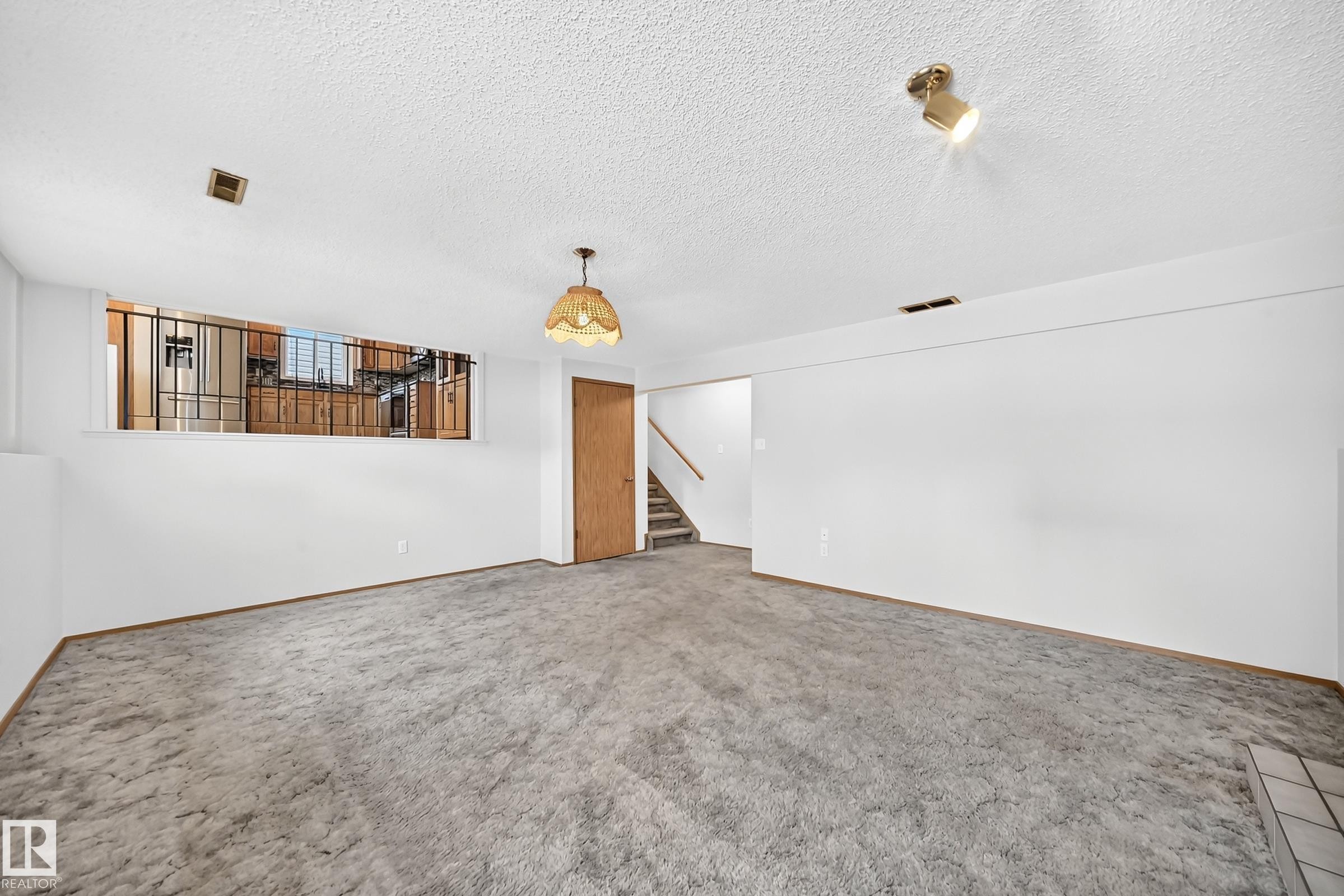 Spacious open living area with concrete flooring, recessed ceiling lighting, and a gold pendant fixture - 14519 32 Street Nw, Edmonton, AB