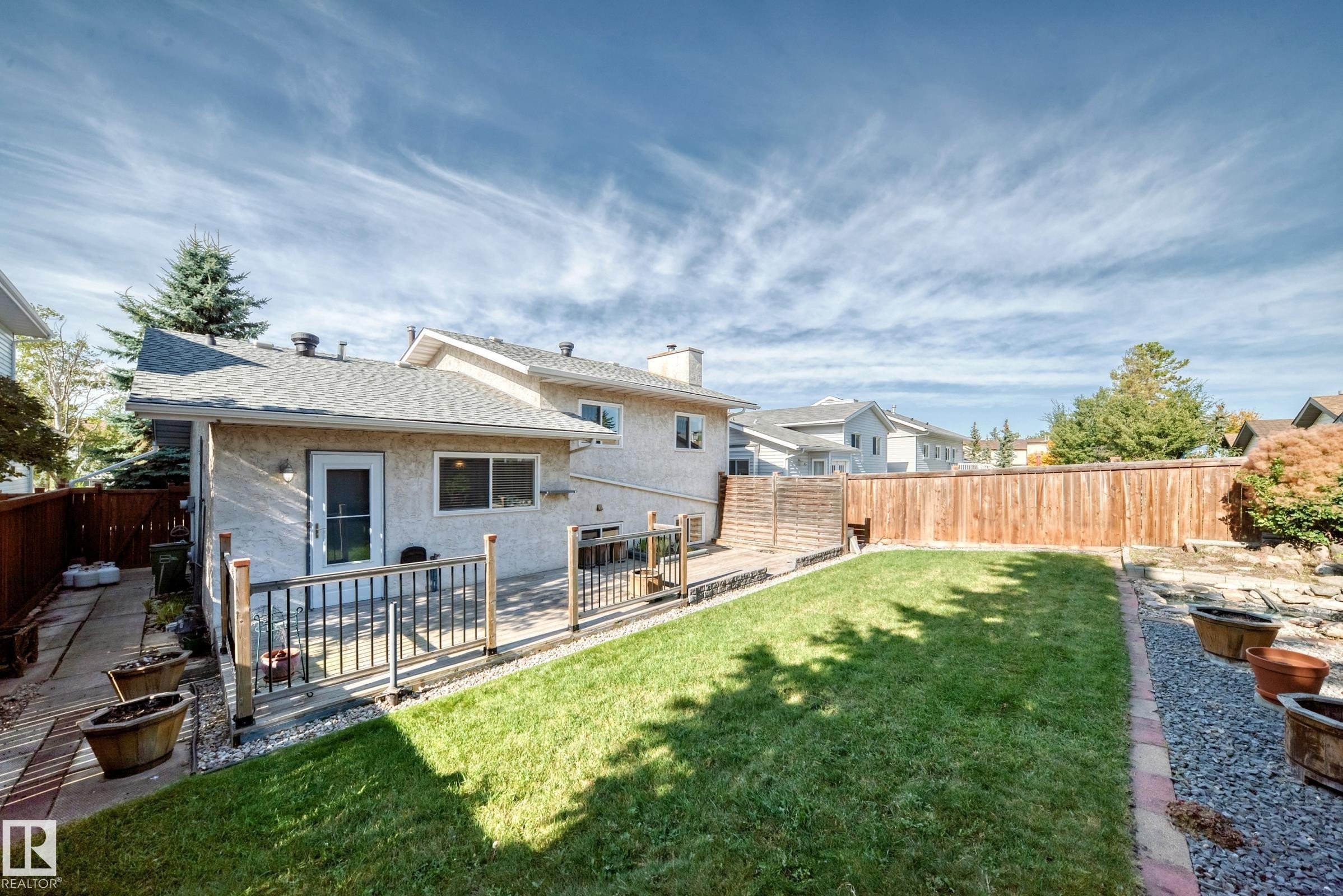 Backyard featuring a wood deck with black metal railings, a manicured lawn, a gravel border, and a wood privacy fence - 14519 32 Street Nw, Edmonton, AB