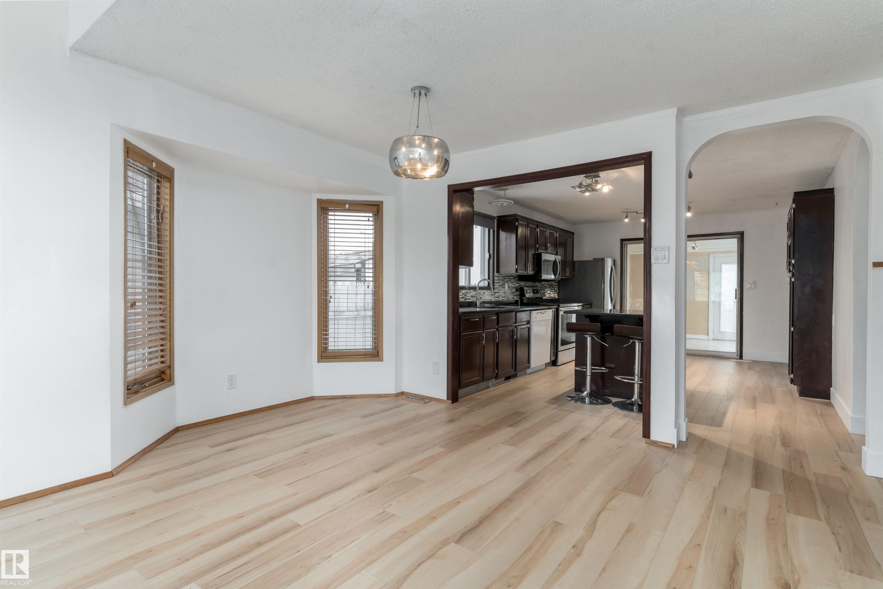Light wood-finish flooring, bay window with wood trim, contemporary pendant lighting, dark wood-finish cabinetry, stainless steel appliances - 18739 72 Avenue Nw, Edmonton, AB