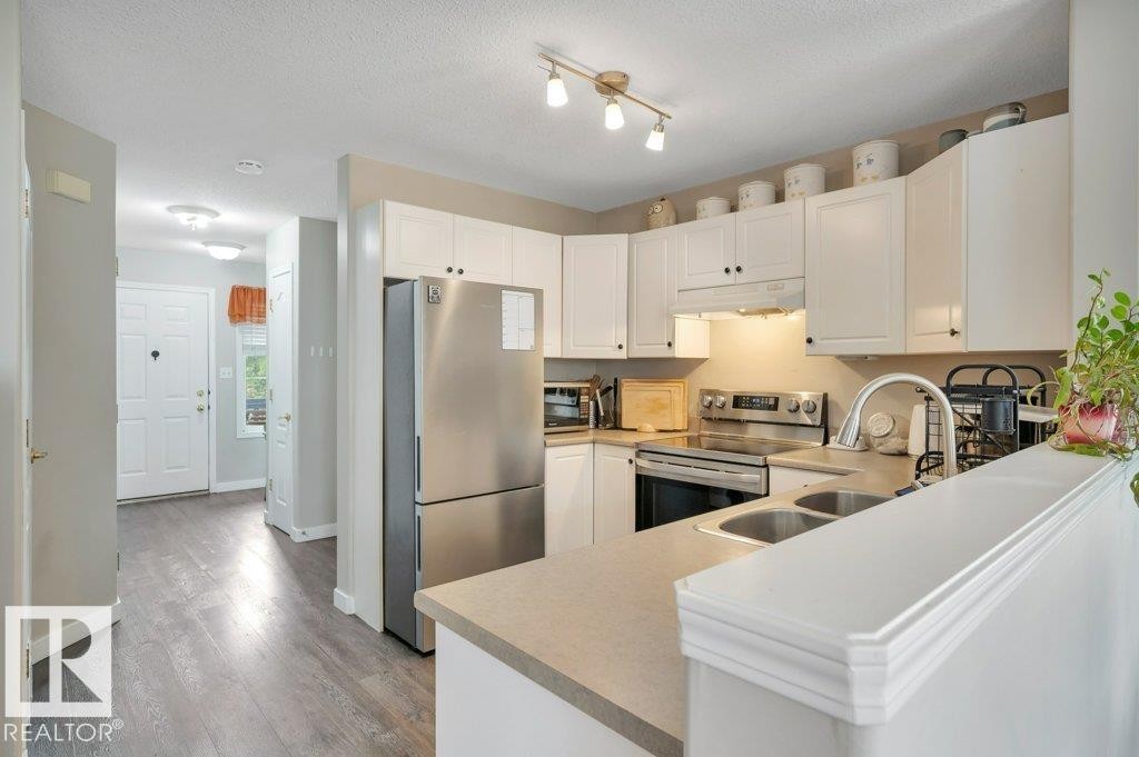 Kitchen featuring white cabinetry, stainless steel appliances, dual basin sink, and a peninsula countertop - 11448 169 Avenue Nw, Edmonton, AB