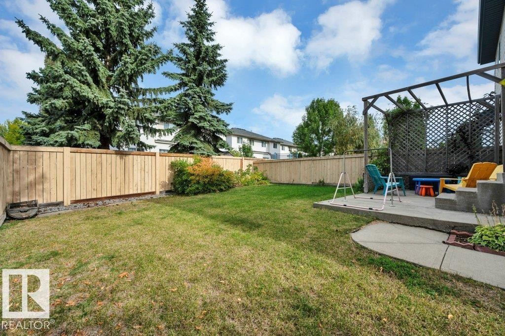 Expansive backyard with a manicured lawn, wood privacy fencing, and a concrete patio featuring a pergola with lattice detailing - 11448 169 Avenue Nw, Edmonton, AB